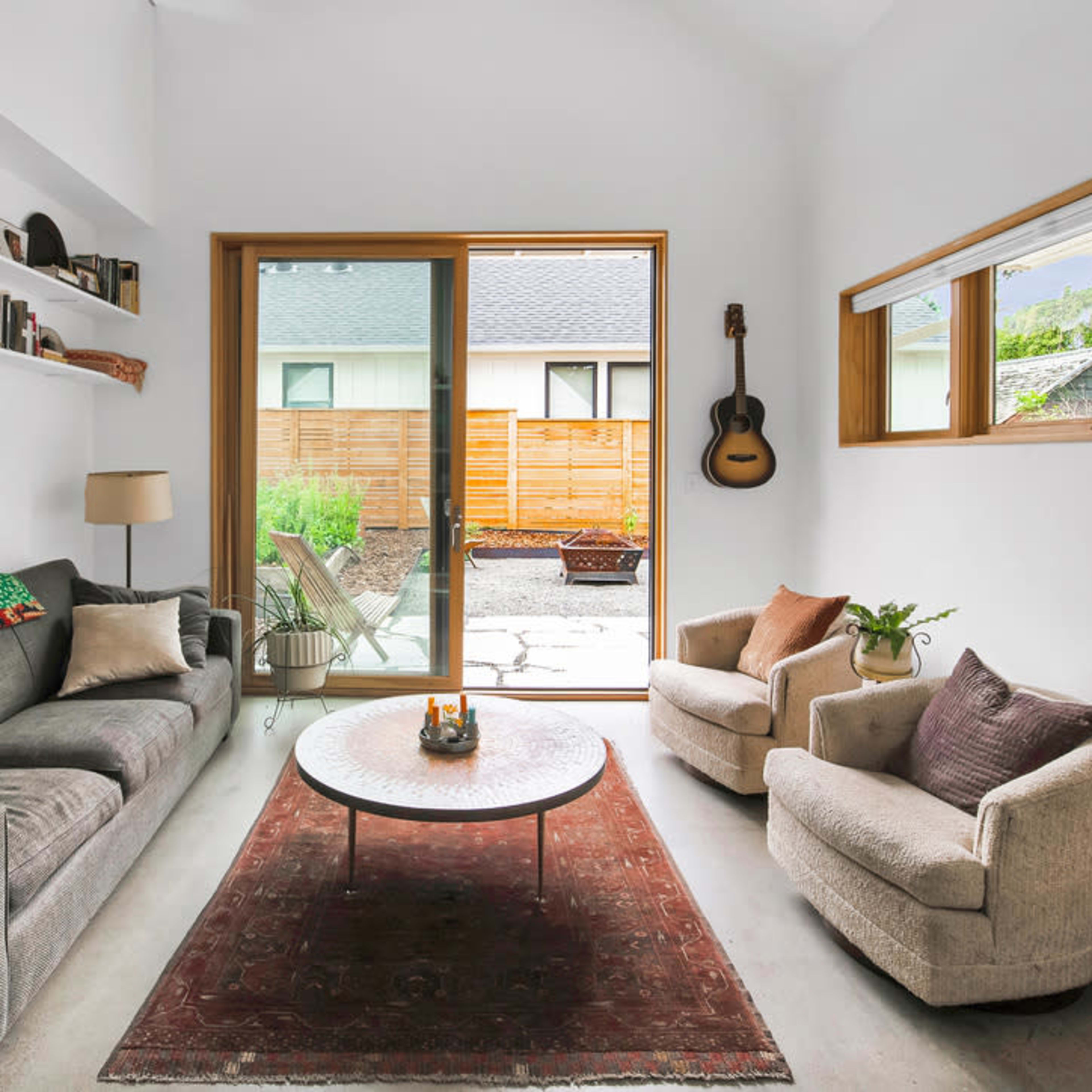 A modern living room with a gray sofa, two armchairs, a round coffee table, and large windows that open to a courtyard.