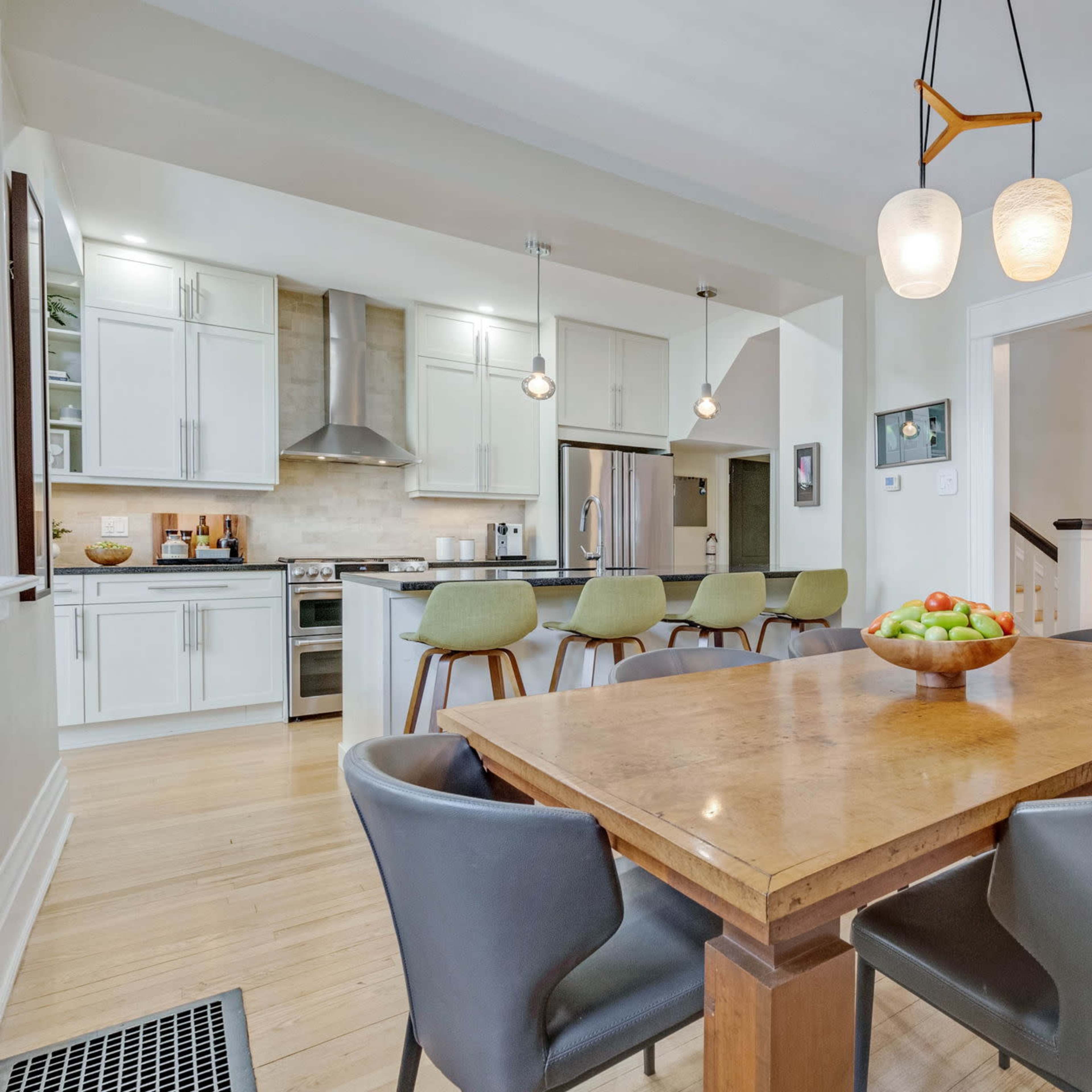 A modern kitchen and dining area featuring a wooden table with gray chairs, pendant lighting, and stainless steel appliances.