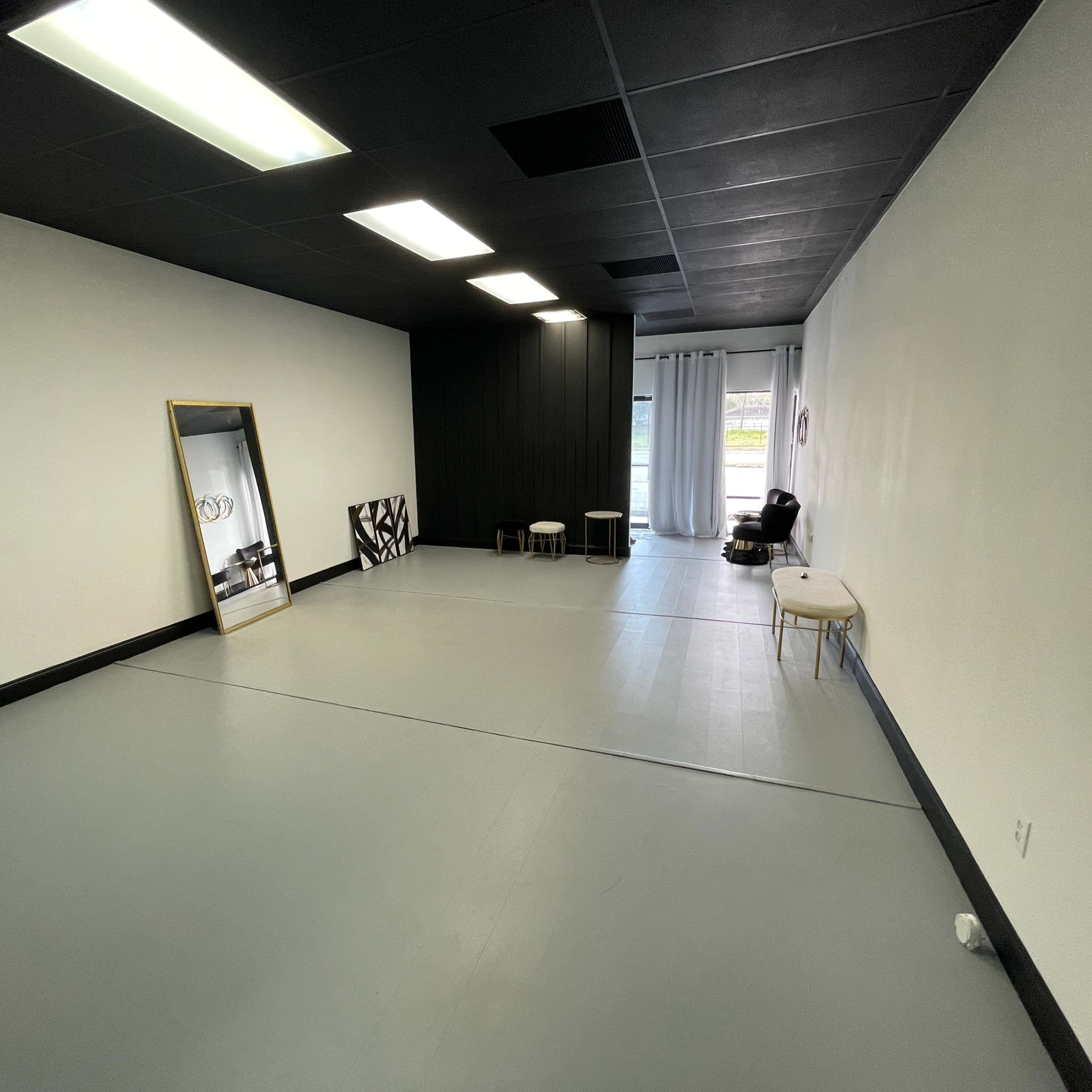 An empty, well-lit room with gray flooring, a large mirror, two small stools, and a curtain window.