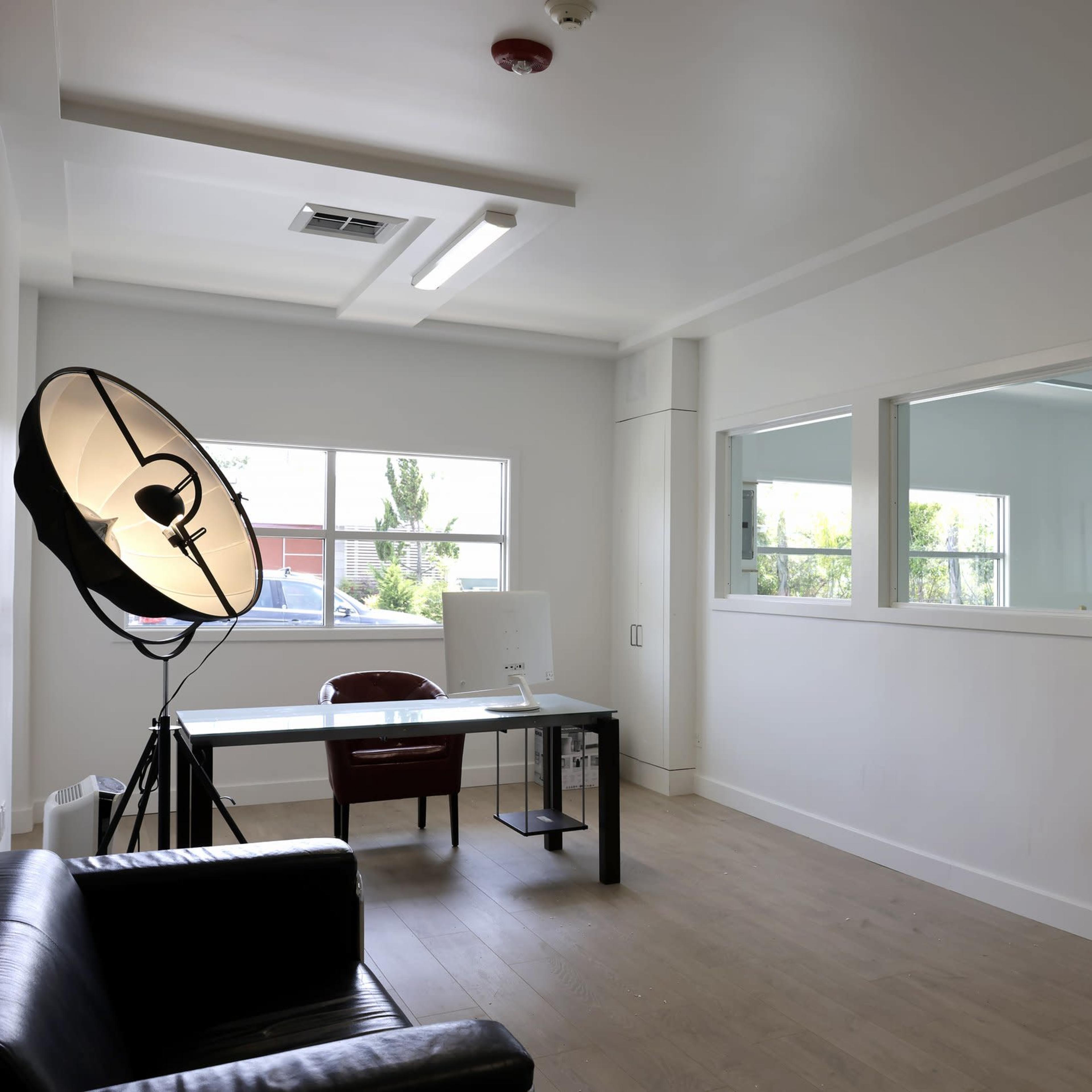 A bright, minimalist office space with a desk, a chair, and a large floor lamp, alongside a window offering natural light.