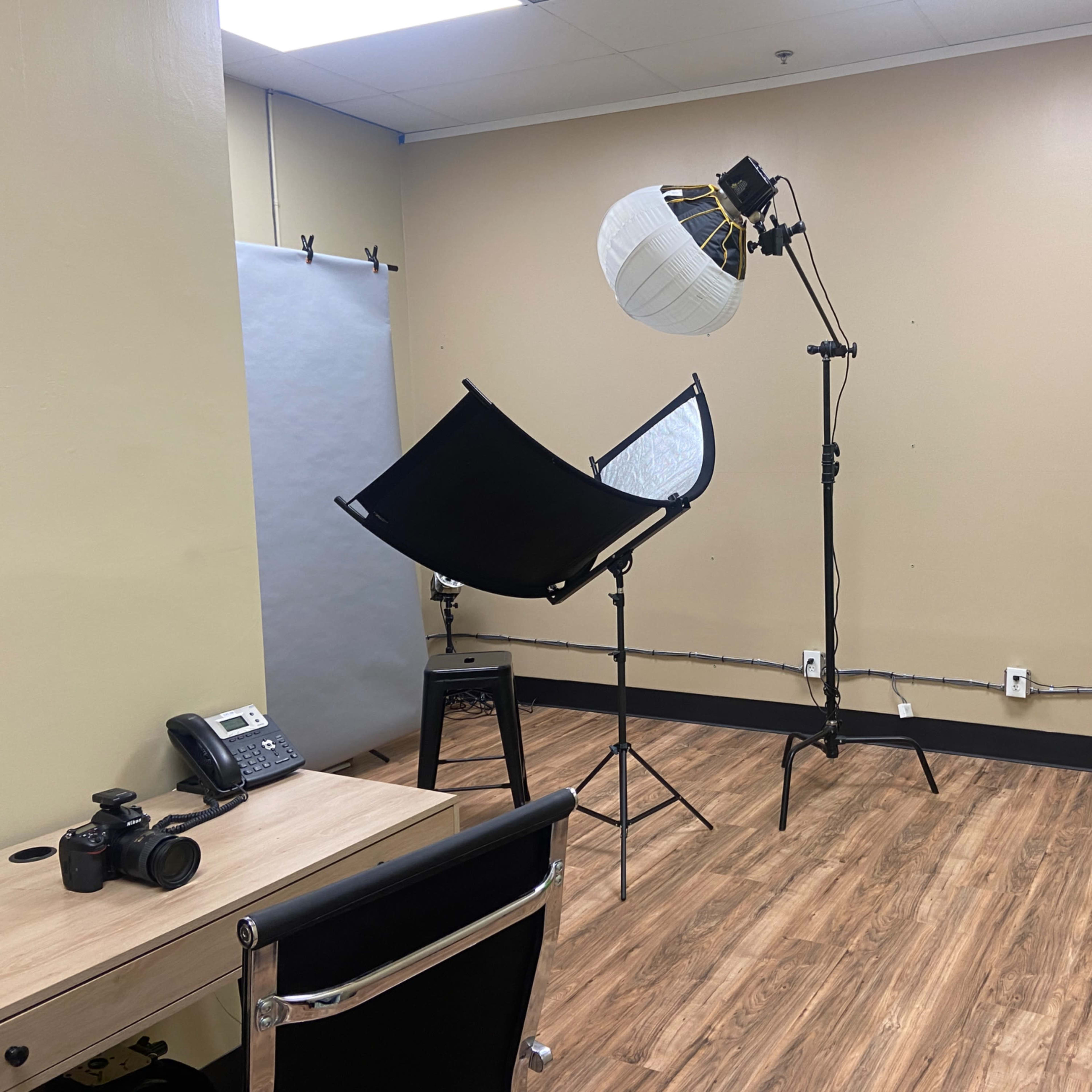 A small studio space equipped with photography lights, a green screen, a camera, a phone, and a table.