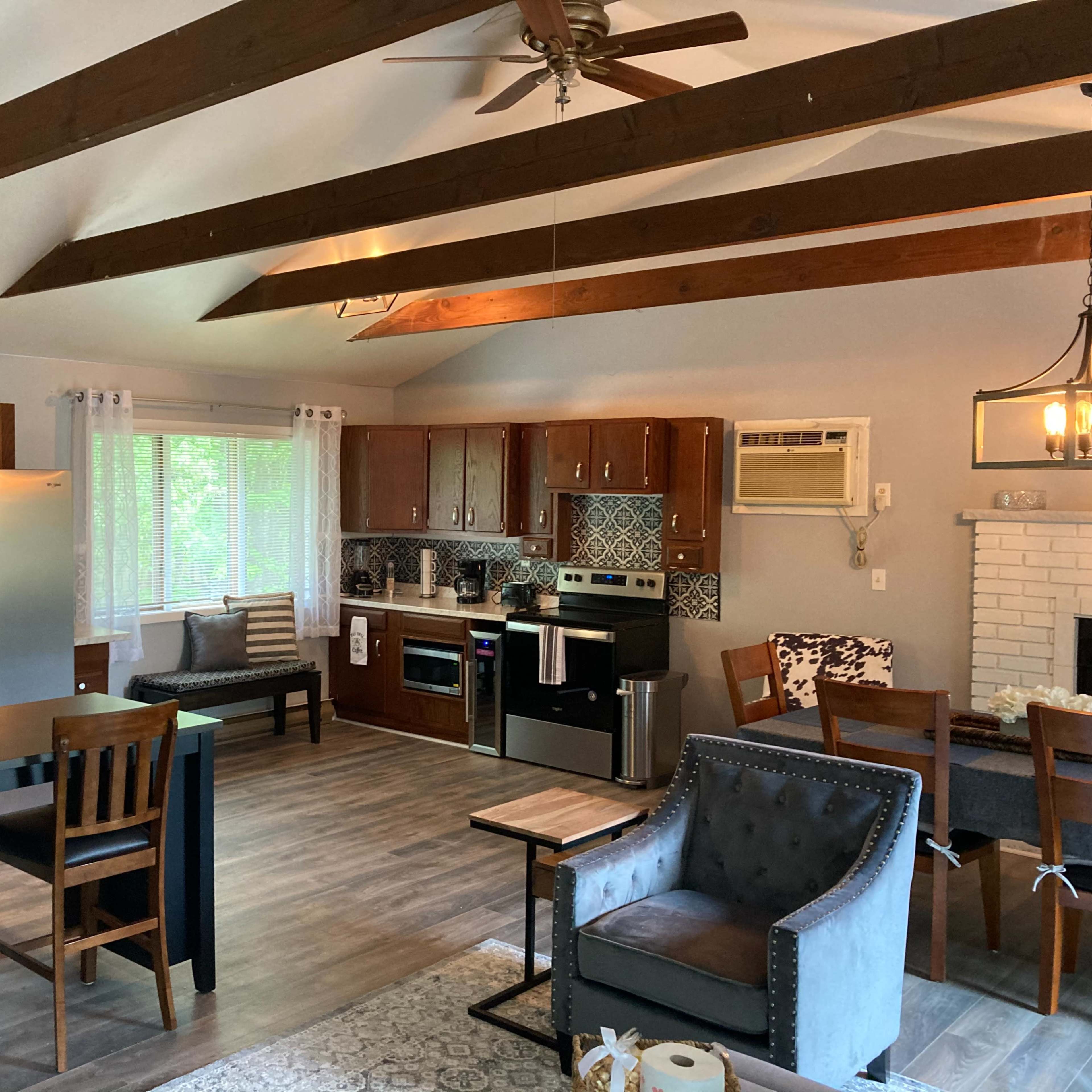 A modern open-concept kitchen and living area featuring wooden beams, a sink island, and a dining table with chairs.