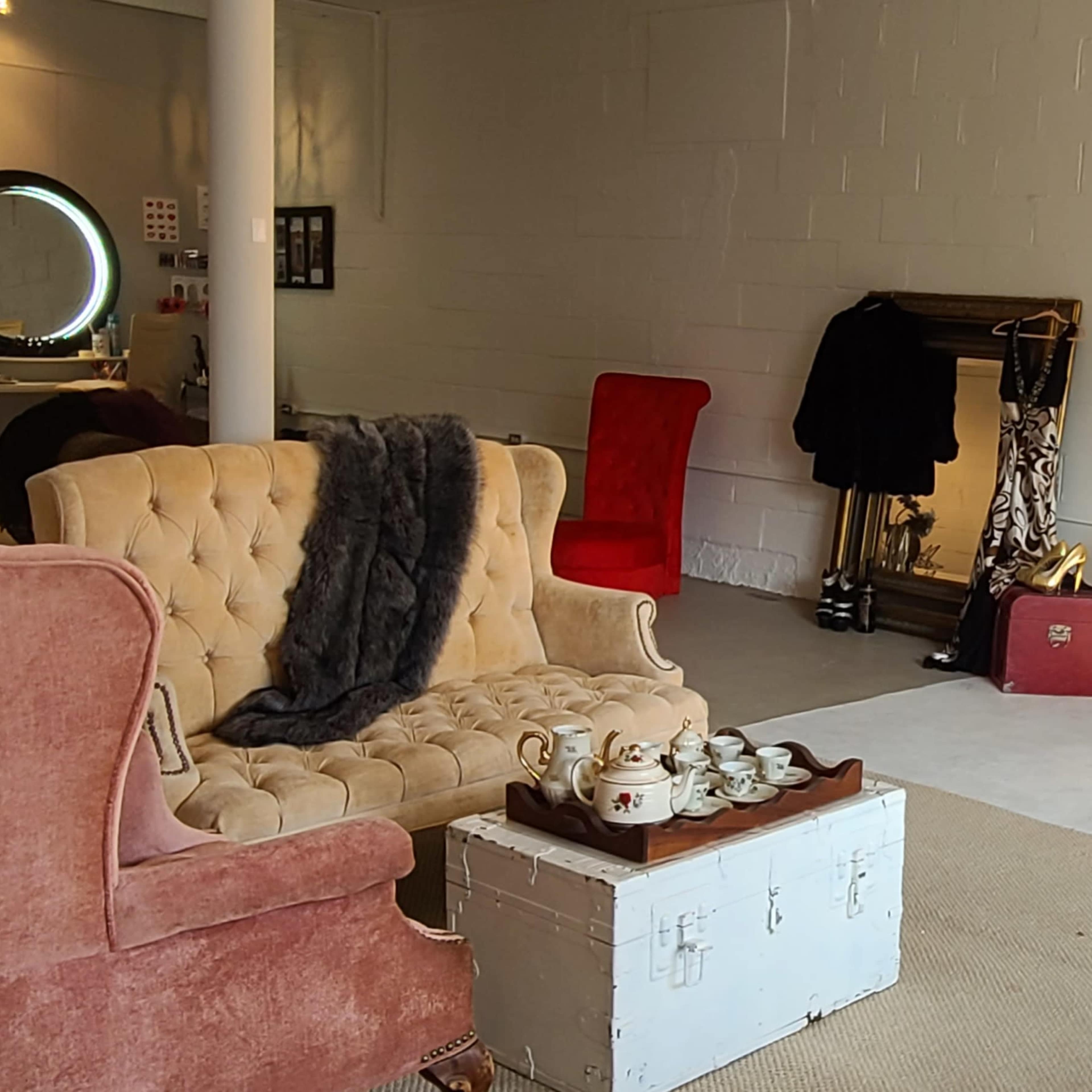 A brightly lit, minimalist room featuring assorted seating, including a pink armchair, a red chair, and a wooden bench, along with a coffee table and a vintage trunk.