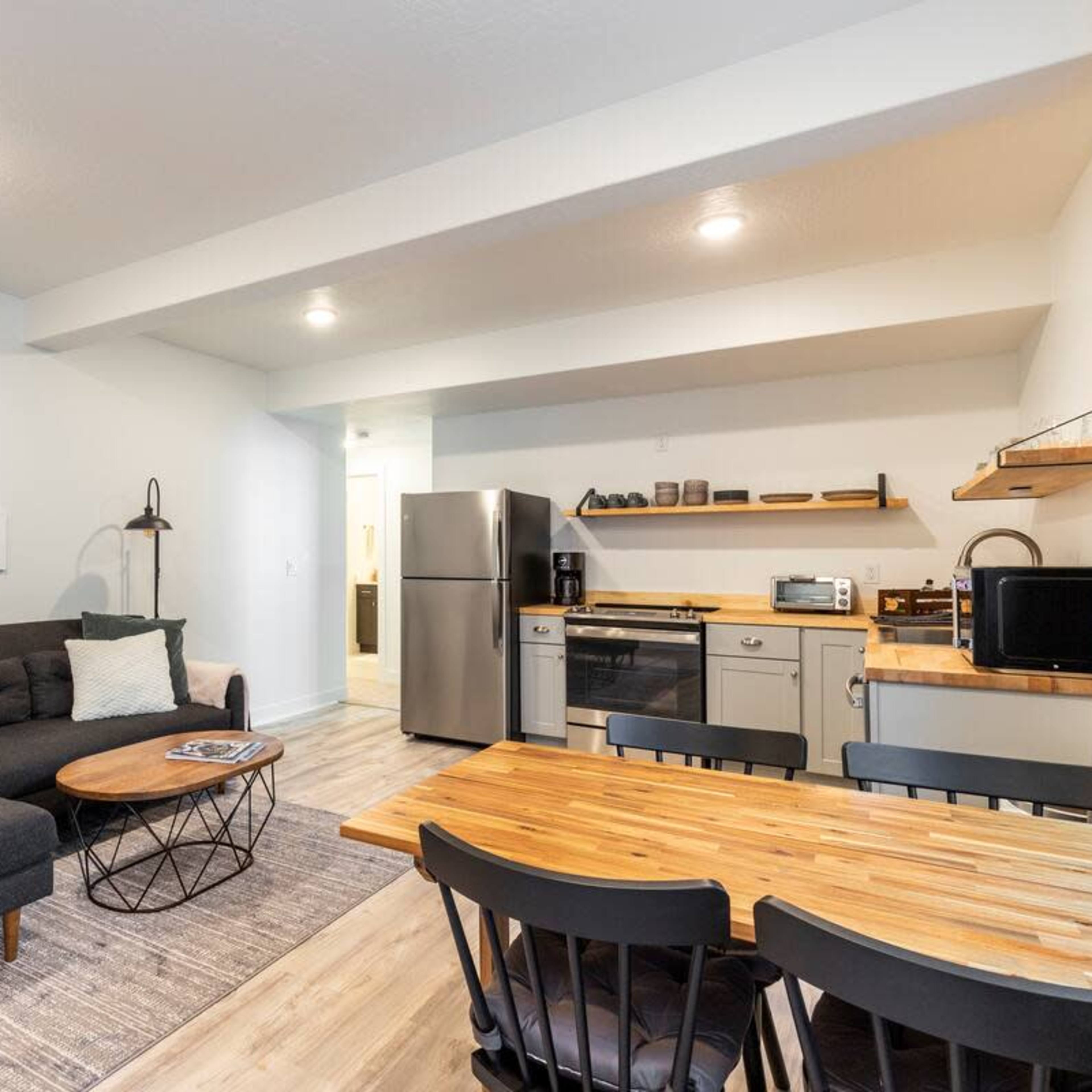 A modern, open-concept living area with a sofa, coffee table, dining table, and kitchen appliances.