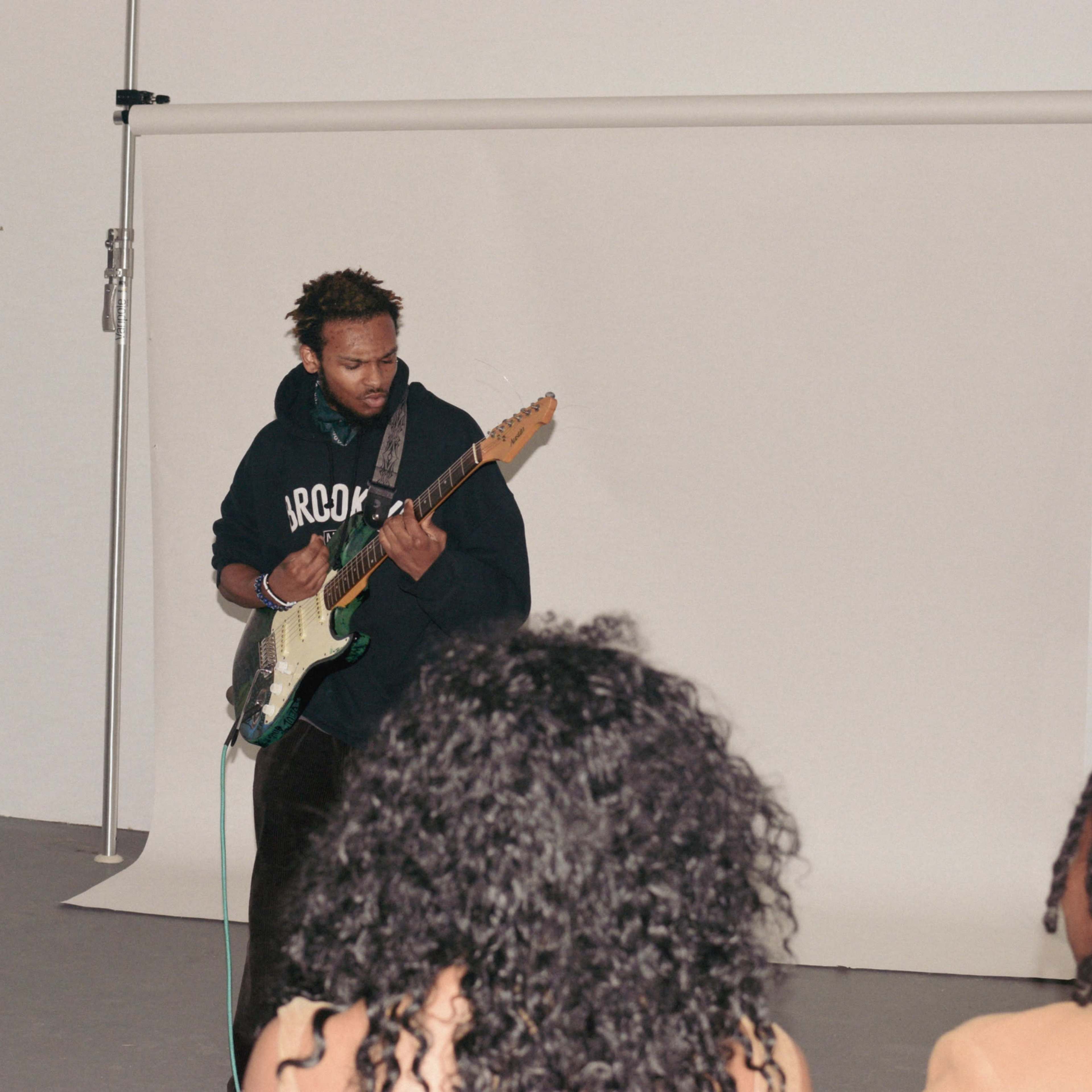 A musician plays an electric guitar on a stage while an audience listens from below.