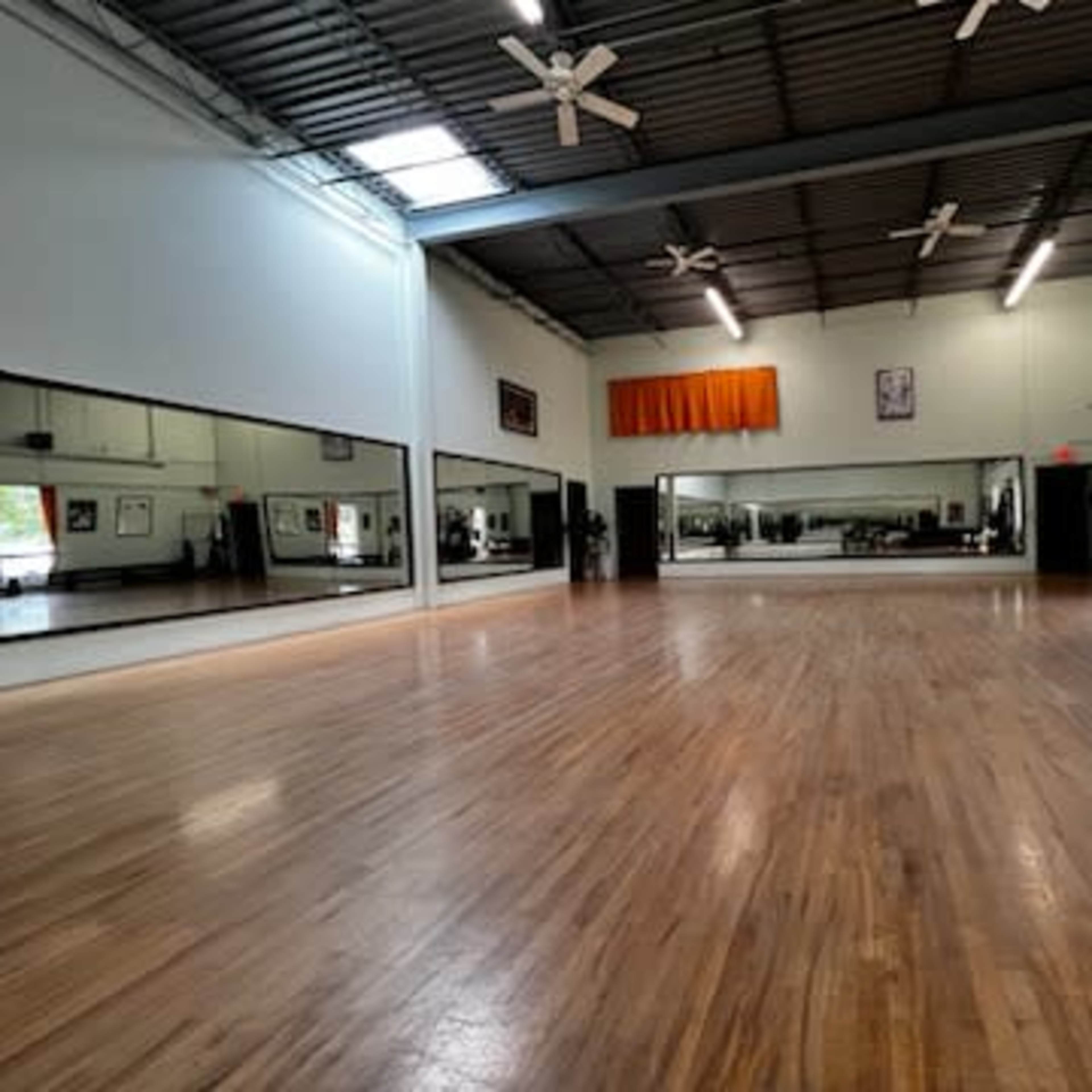 A spacious dance studio featuring wooden floors, large mirrors on one wall, and ceiling fans.