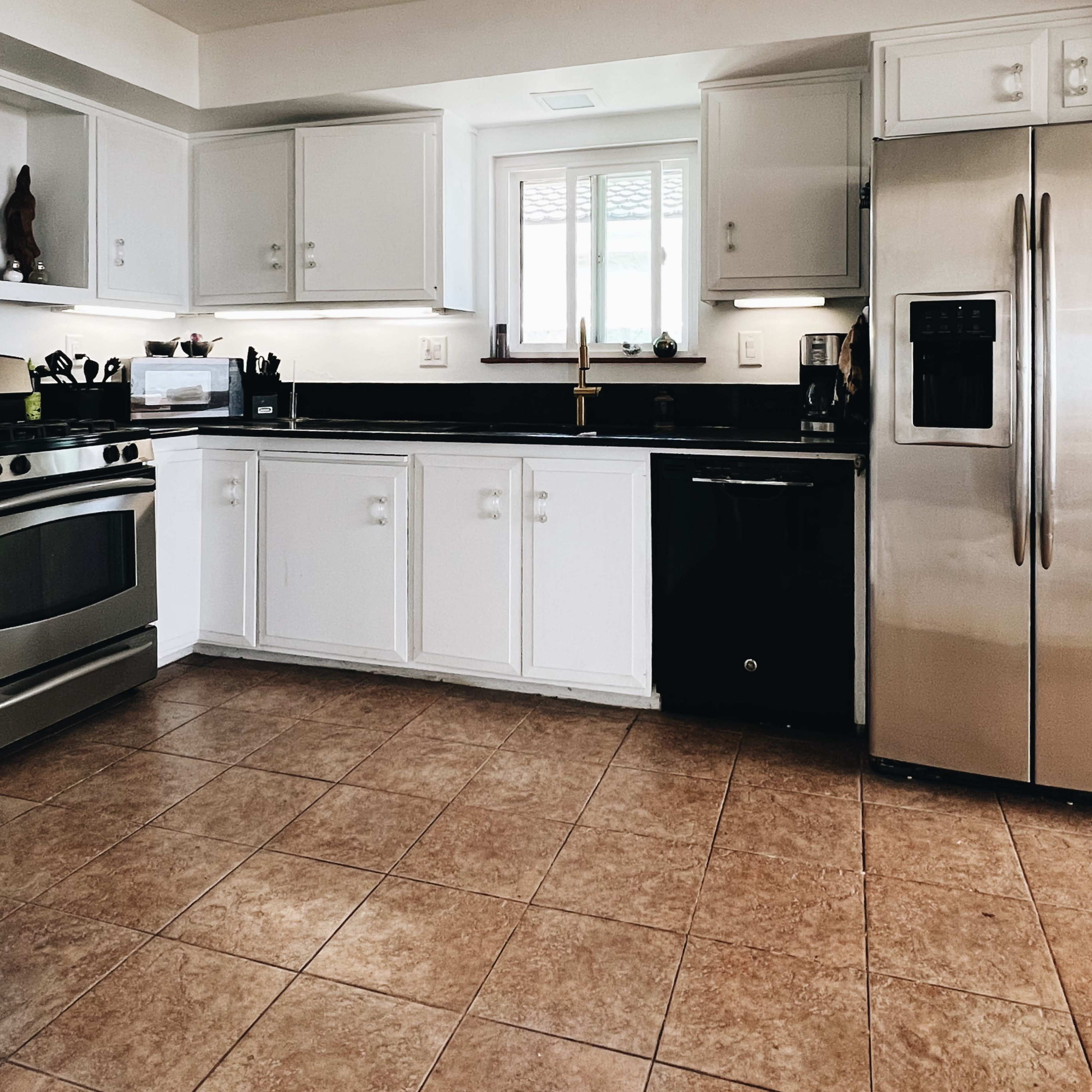 A modern kitchen features white cabinets, a stainless steel refrigerator, a black dishwasher, and a stovetop under a ceiling fan.