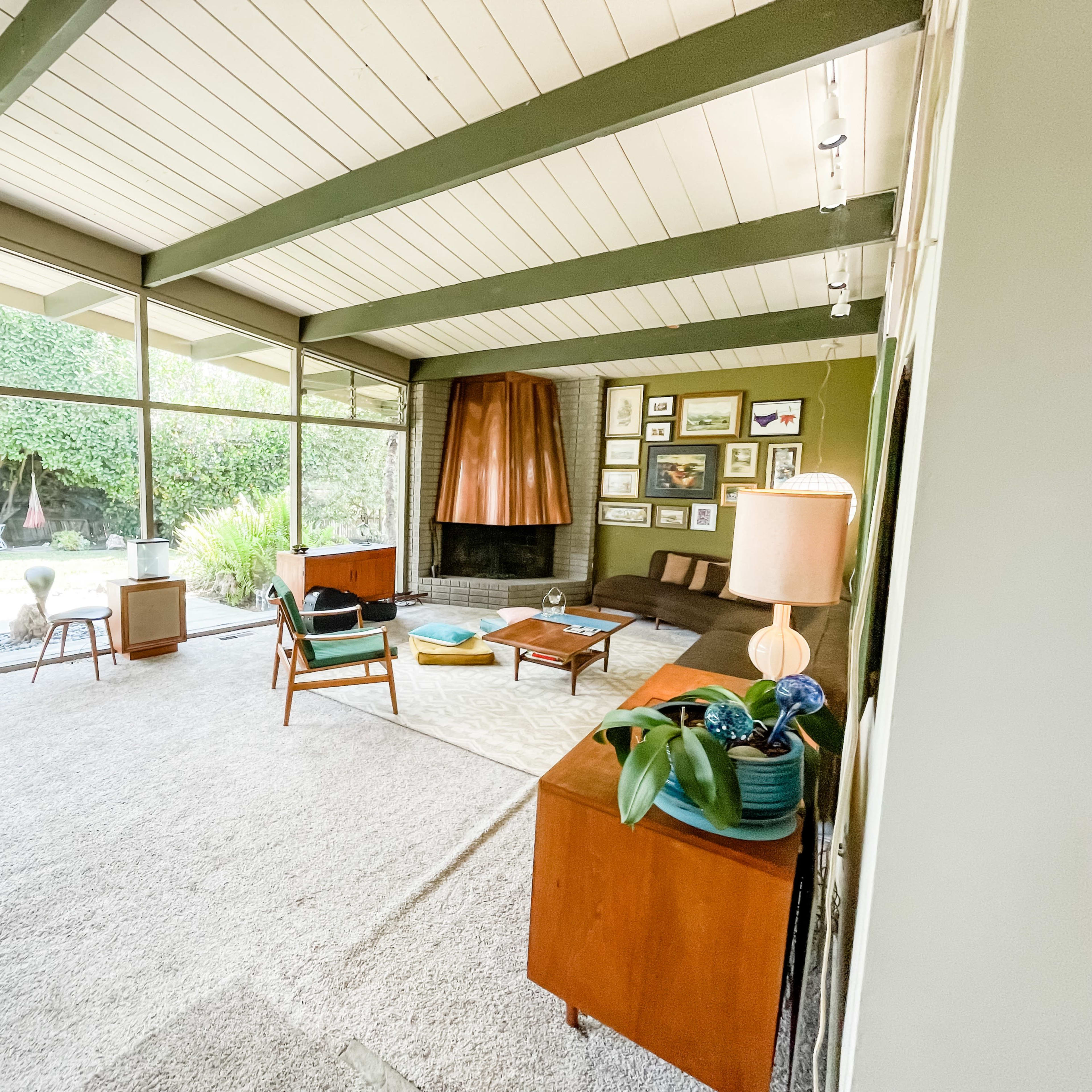 A mid-century modern living room with large glass windows, a stone fireplace, and stylish furniture arrangements.