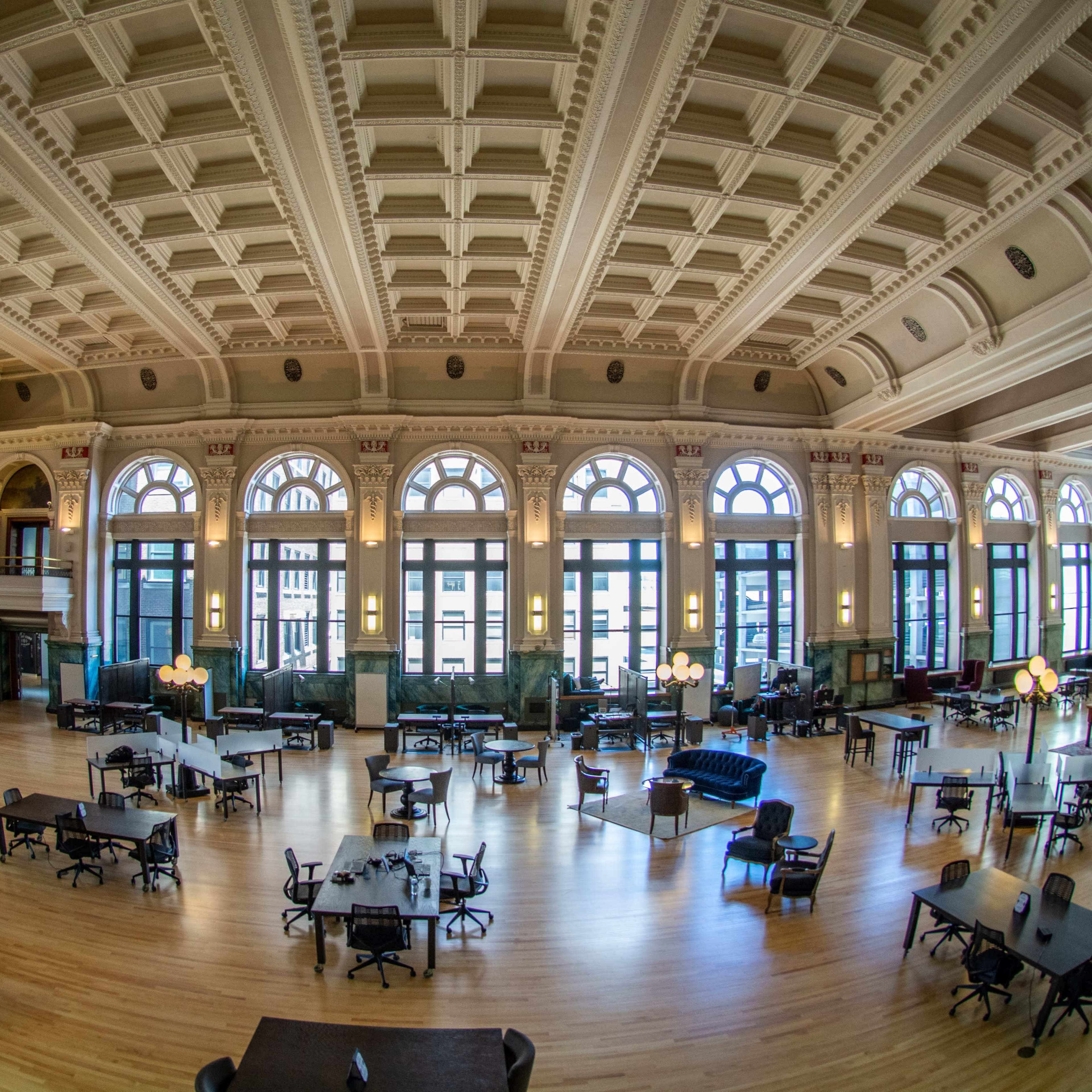 A spacious interior of a public space with high ceilings, large windows, and various seating arrangements, including tables and sofas.