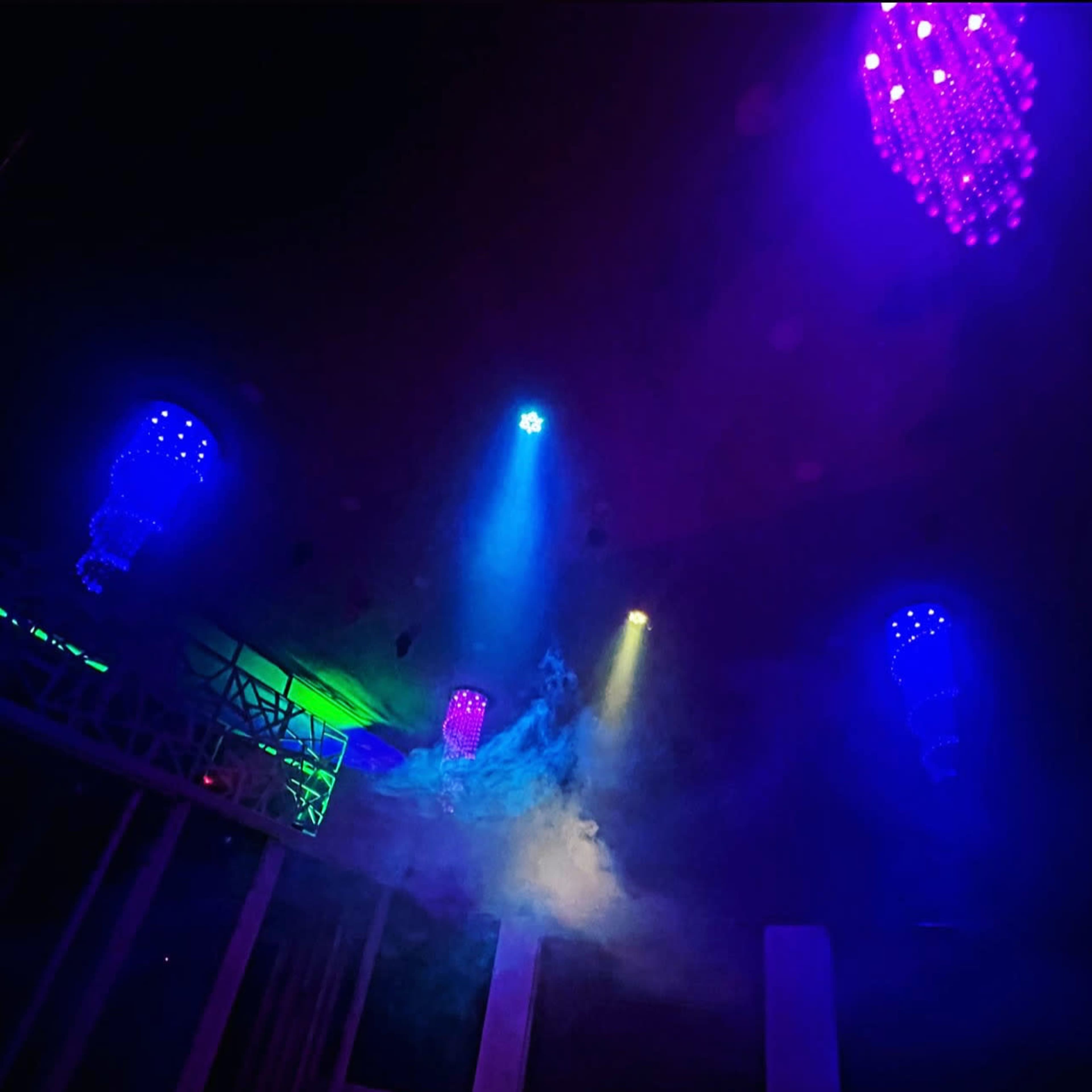 A dimly lit interior features colorful lights and smoke, with chandeliers hanging from the ceiling.