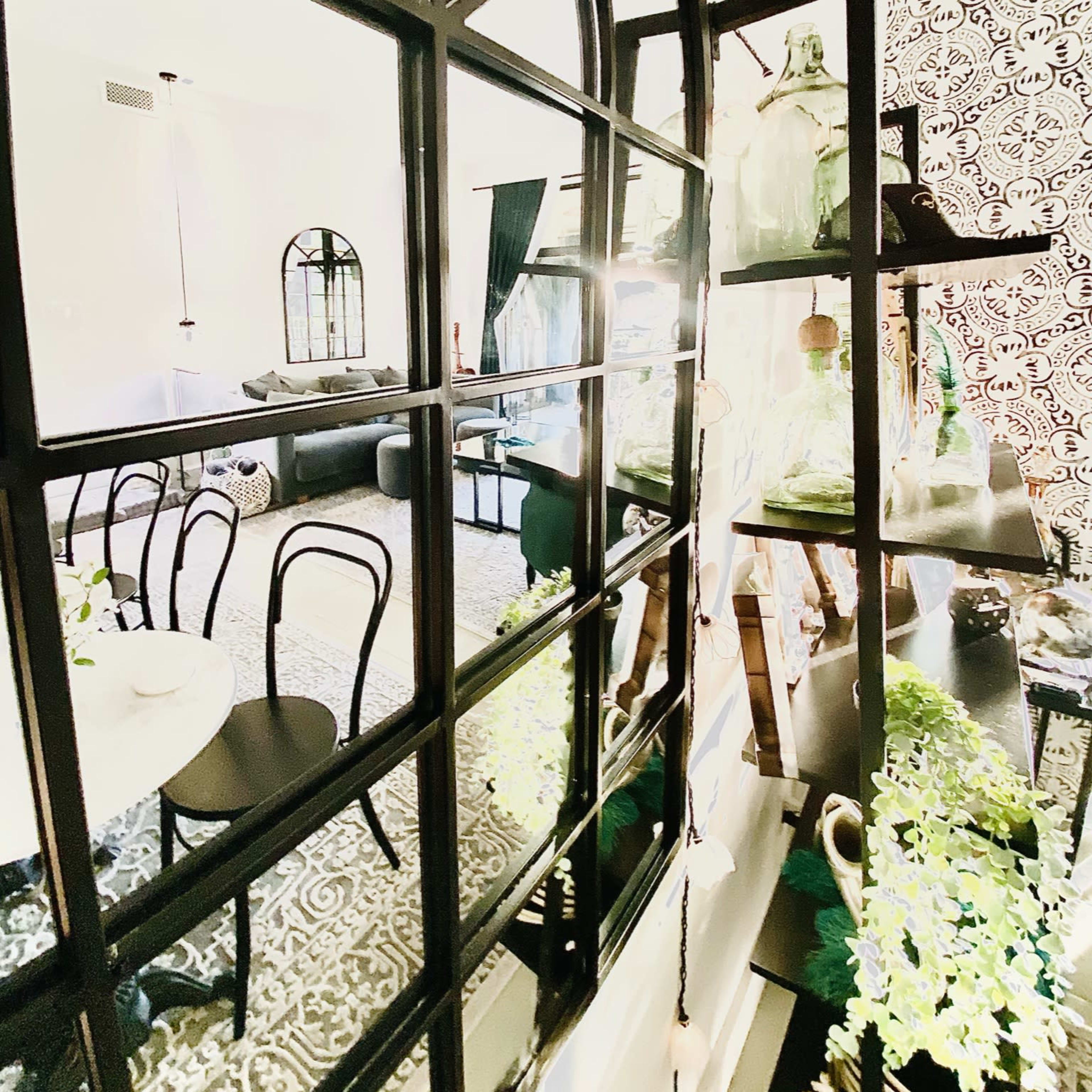 A room featuring a large black-framed mirror reflecting a decorated living space with plants and patterned wallpaper.