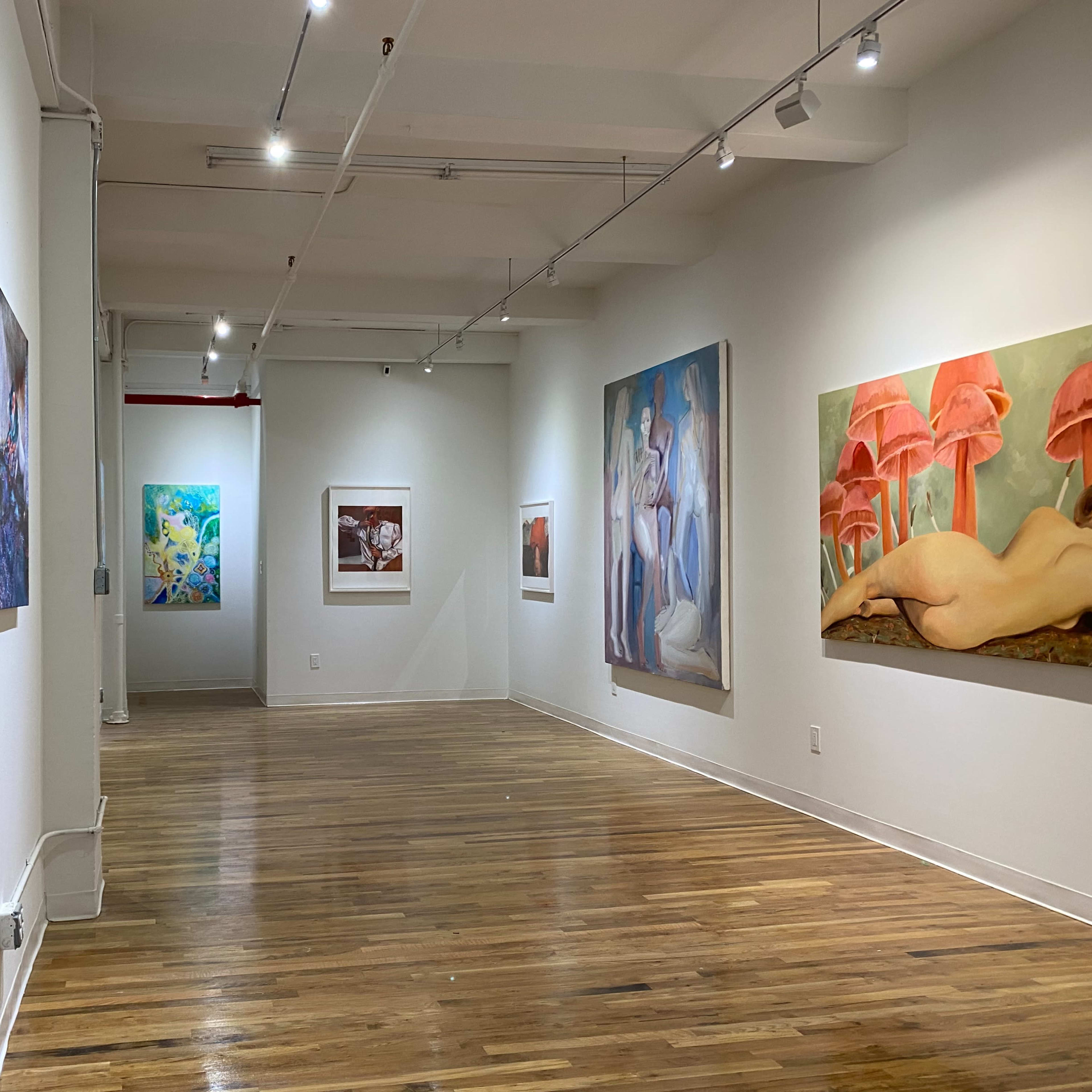 An art gallery with several large paintings on the walls and wooden flooring.