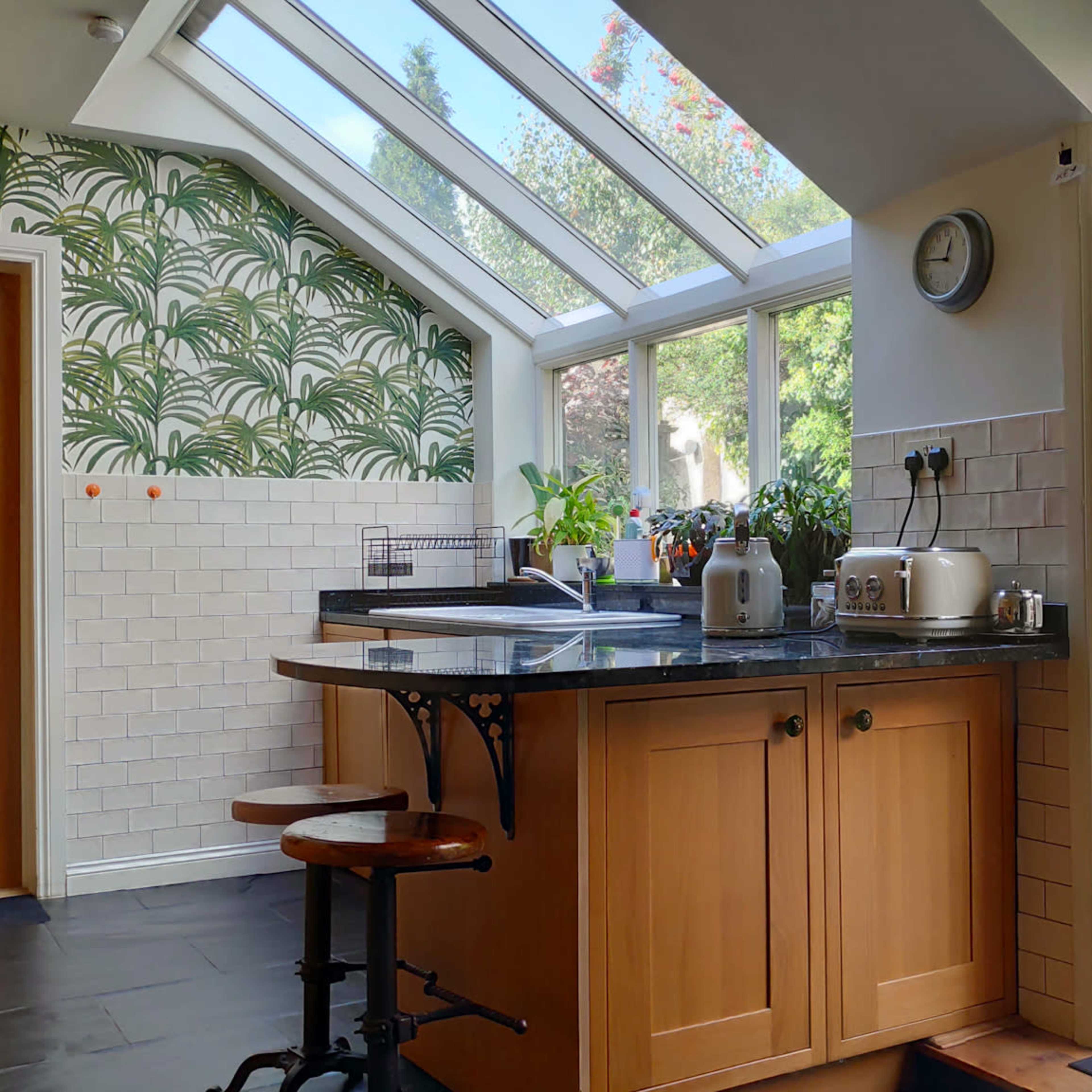 A kitchen with large windows, a wooden countertop, and a glimpse of a garden through an open door.