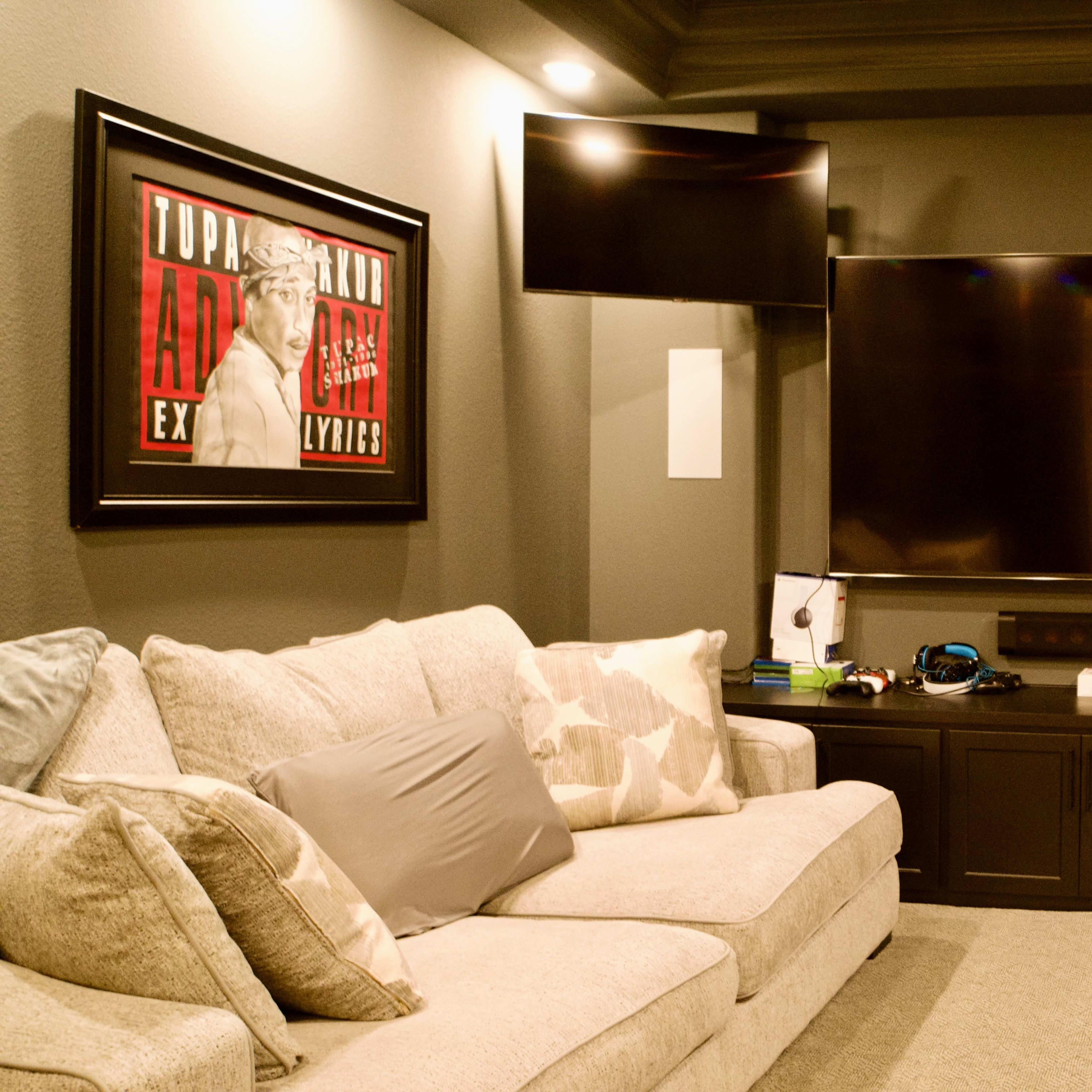 A modern home theater with two large wall-mounted TVs, a dark entertainment unit, and two light-colored sofas.