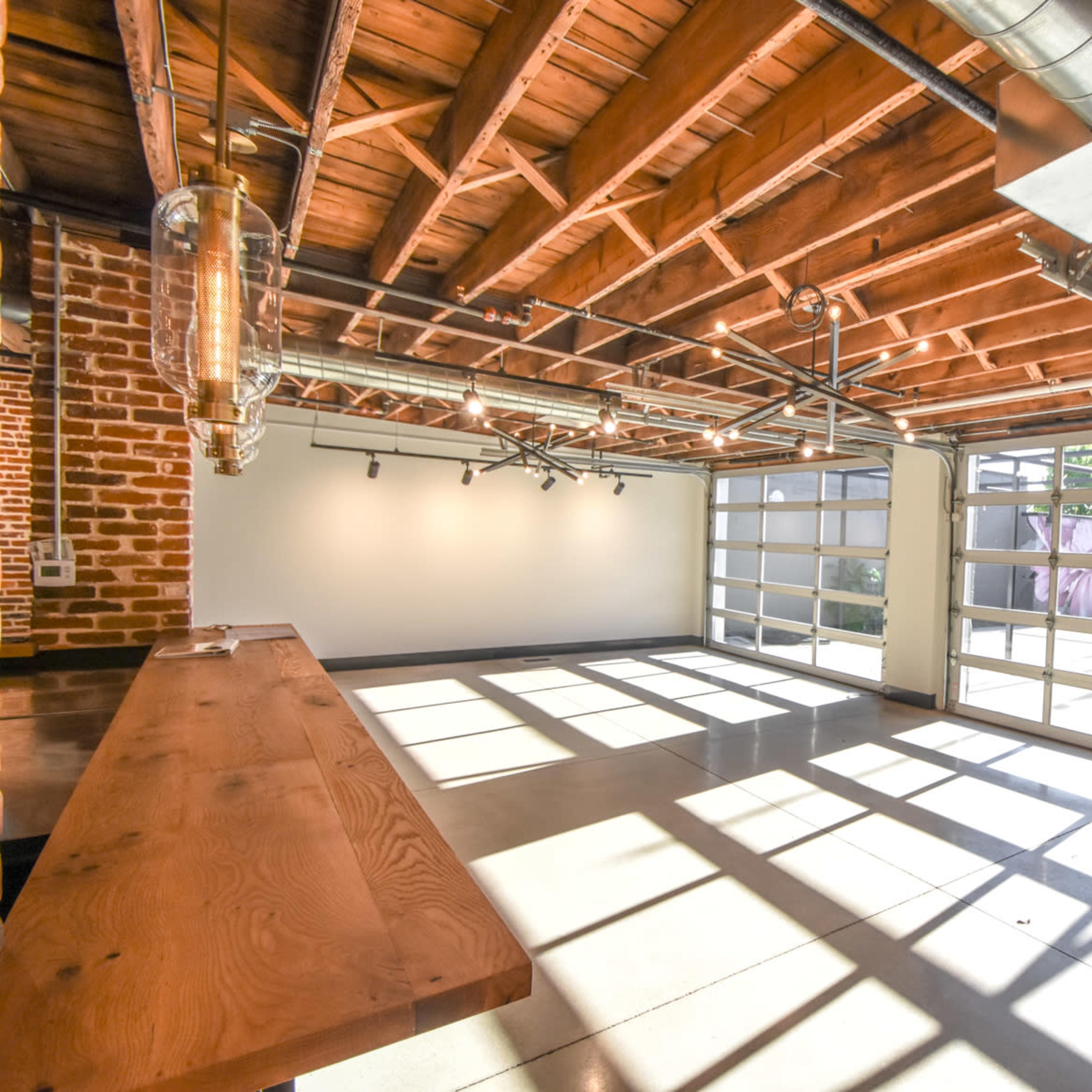 An interior space with exposed wooden beams, industrial-style lighting, and large glass doors that allow natural light to fill the area.