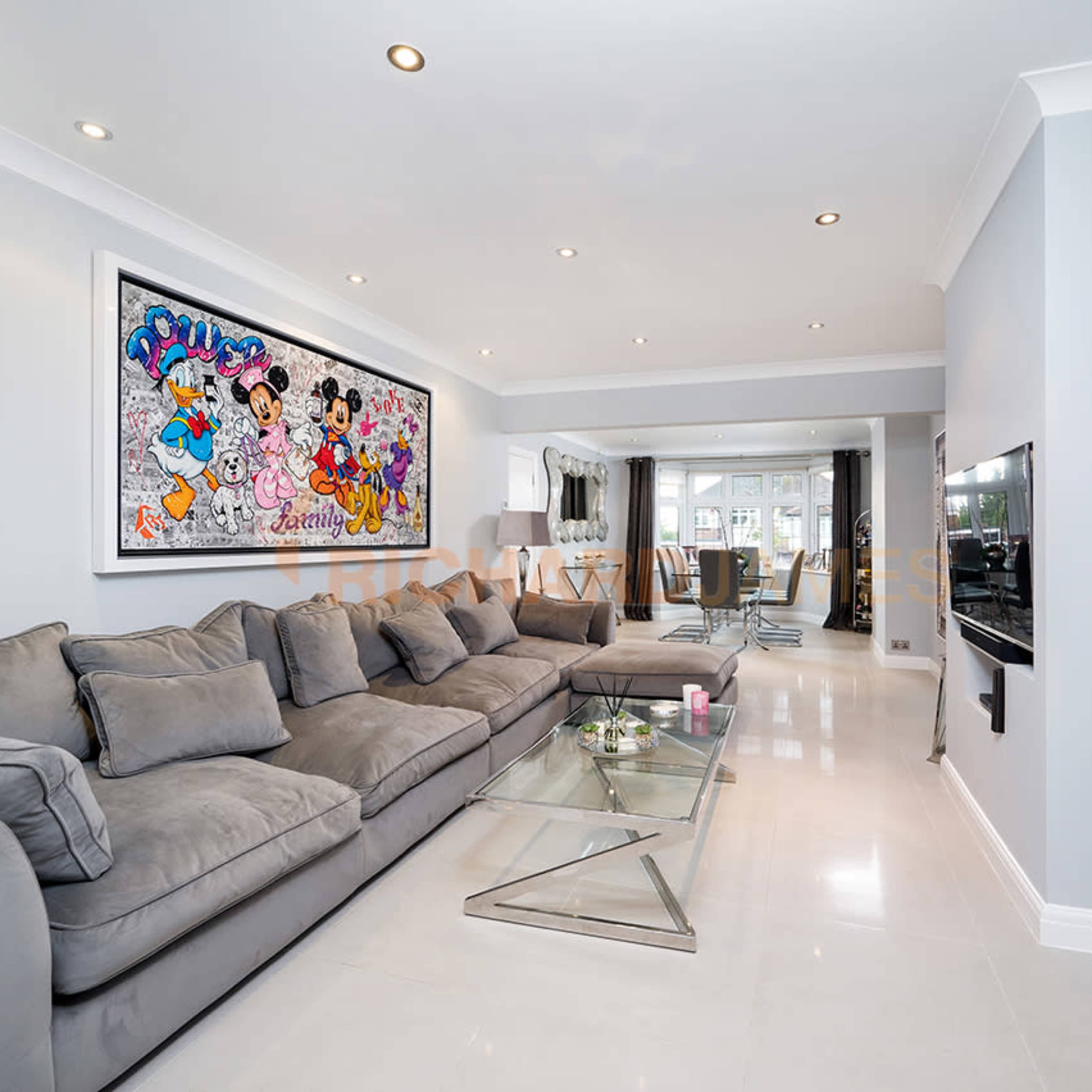 The living room features a large grey sectional sofa, a glass coffee table, and a colorful wall art piece above the couch, with sliding doors leading to an outdoor area.