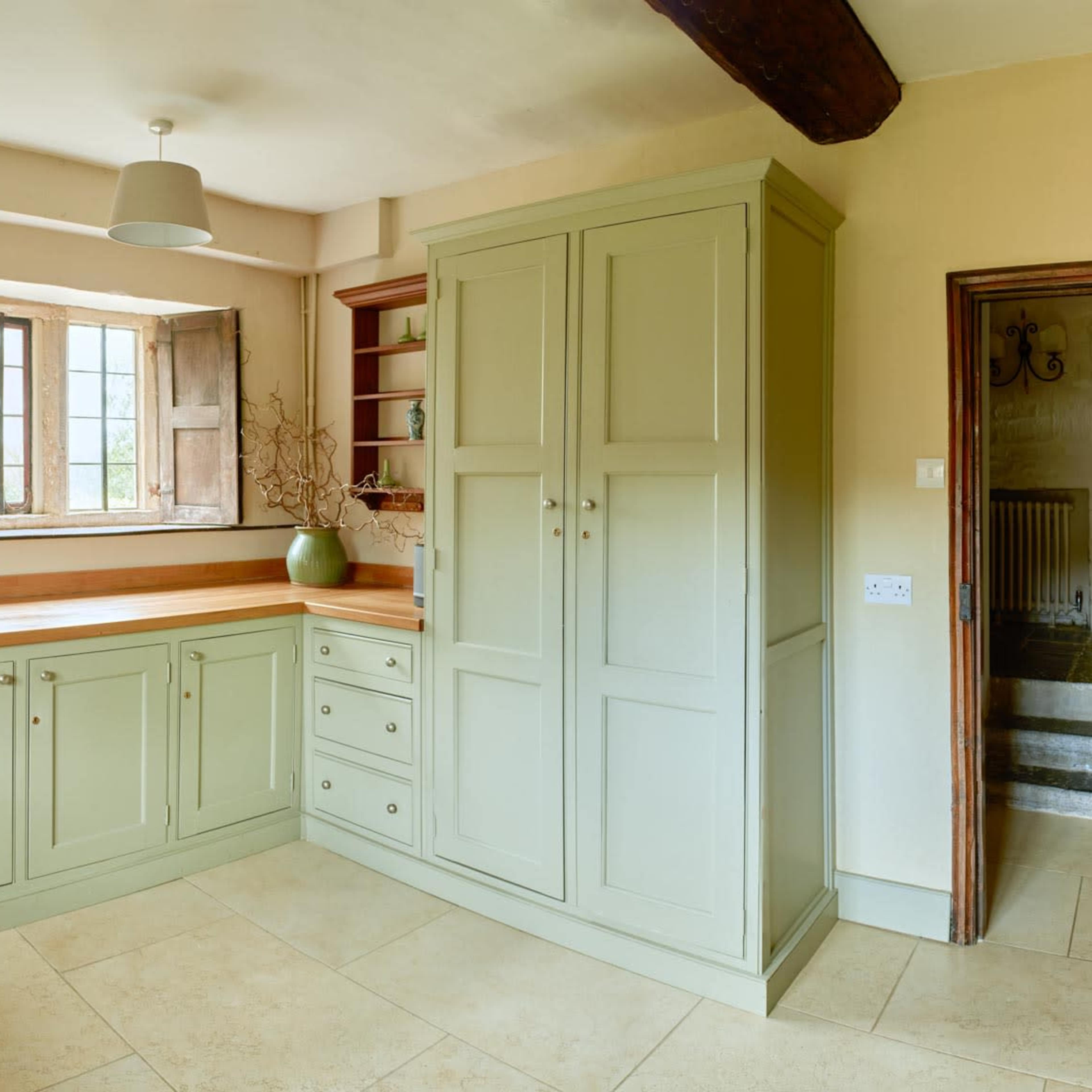 A kitchen with light green cabinetry, wooden countertops, and a large window letting in natural light.