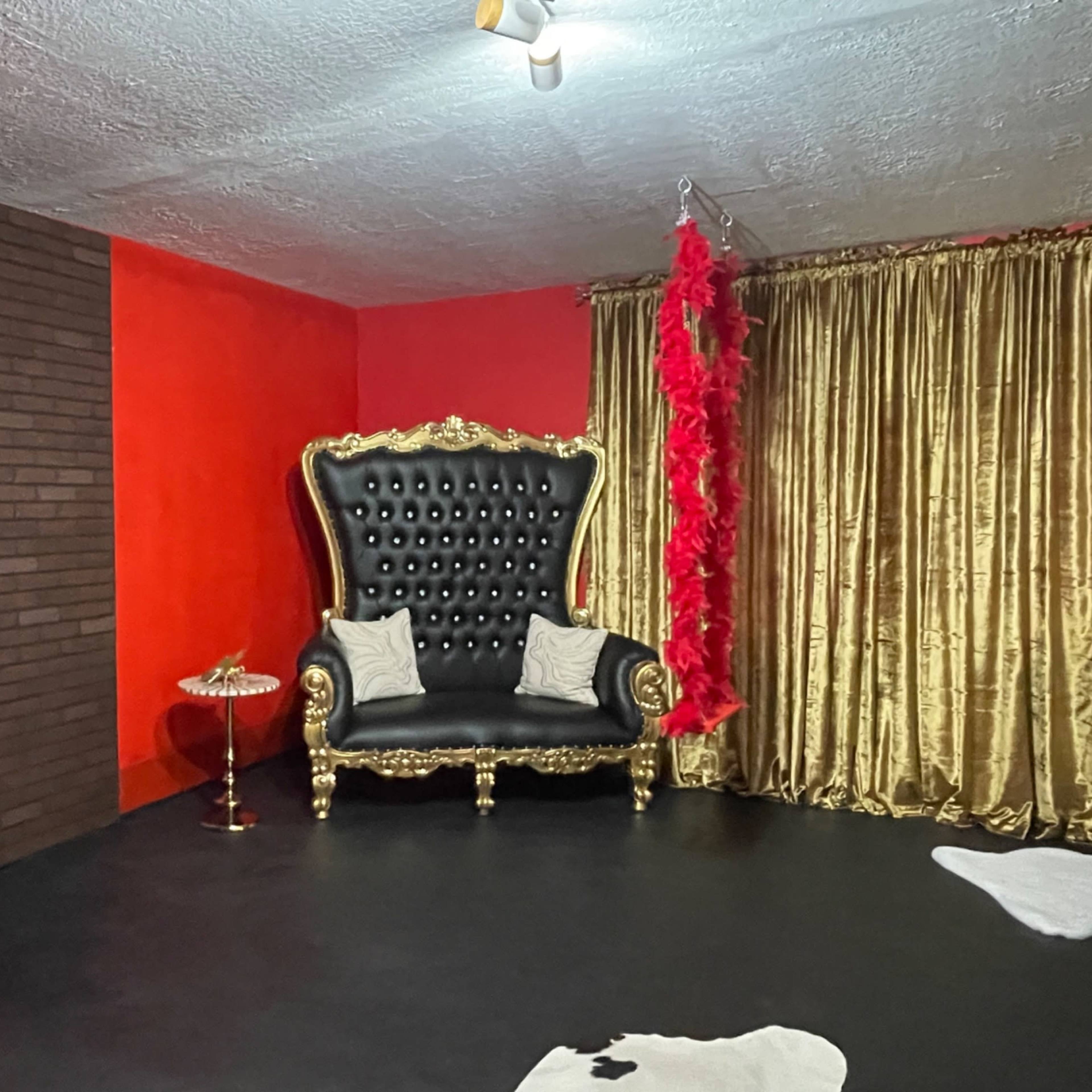 A room featuring a red telephone booth, a black upholstered sofa with gold accents, and gold curtains on a wall.