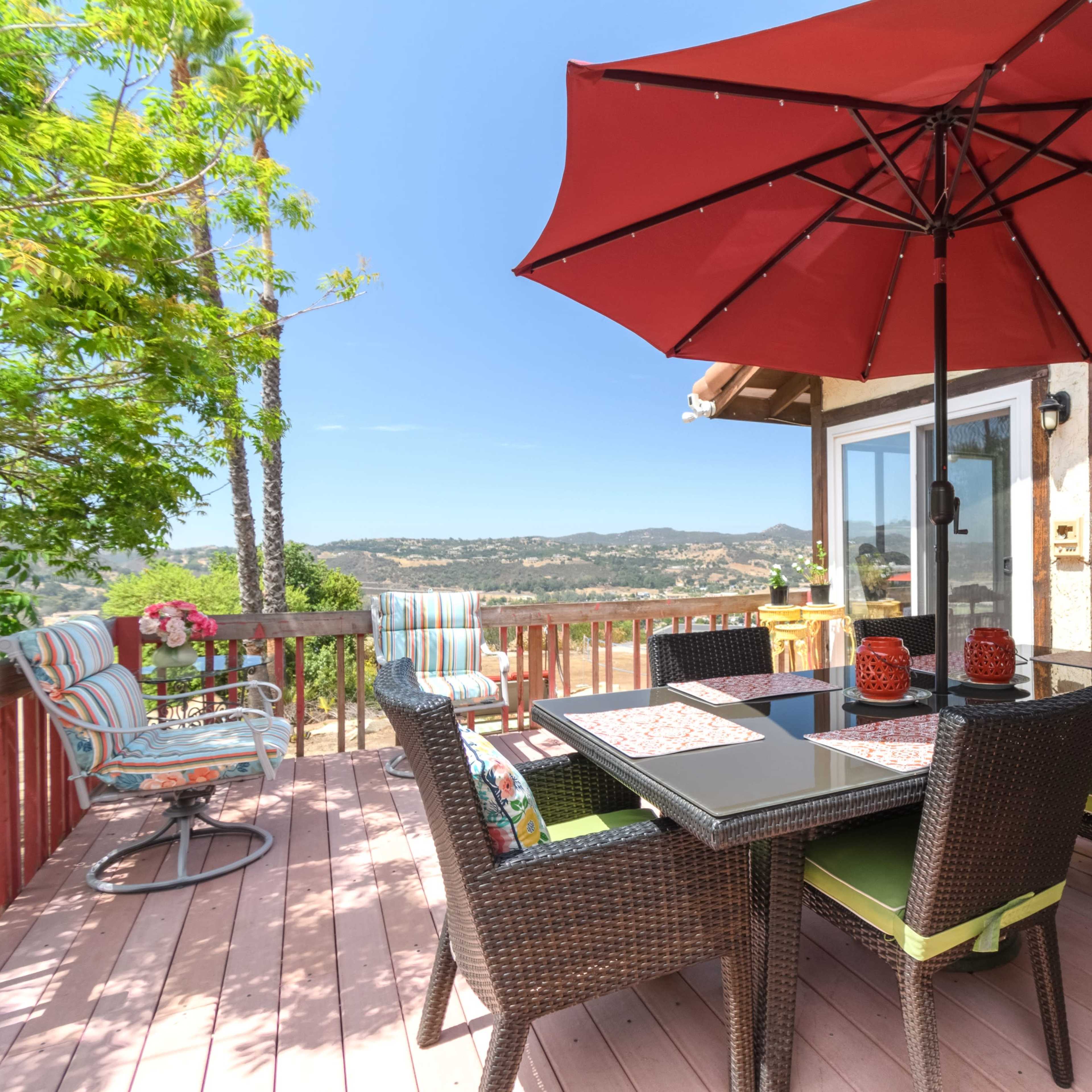 A patio with a dining table, chairs, and an umbrella overlooks a scenic view surrounded by trees.