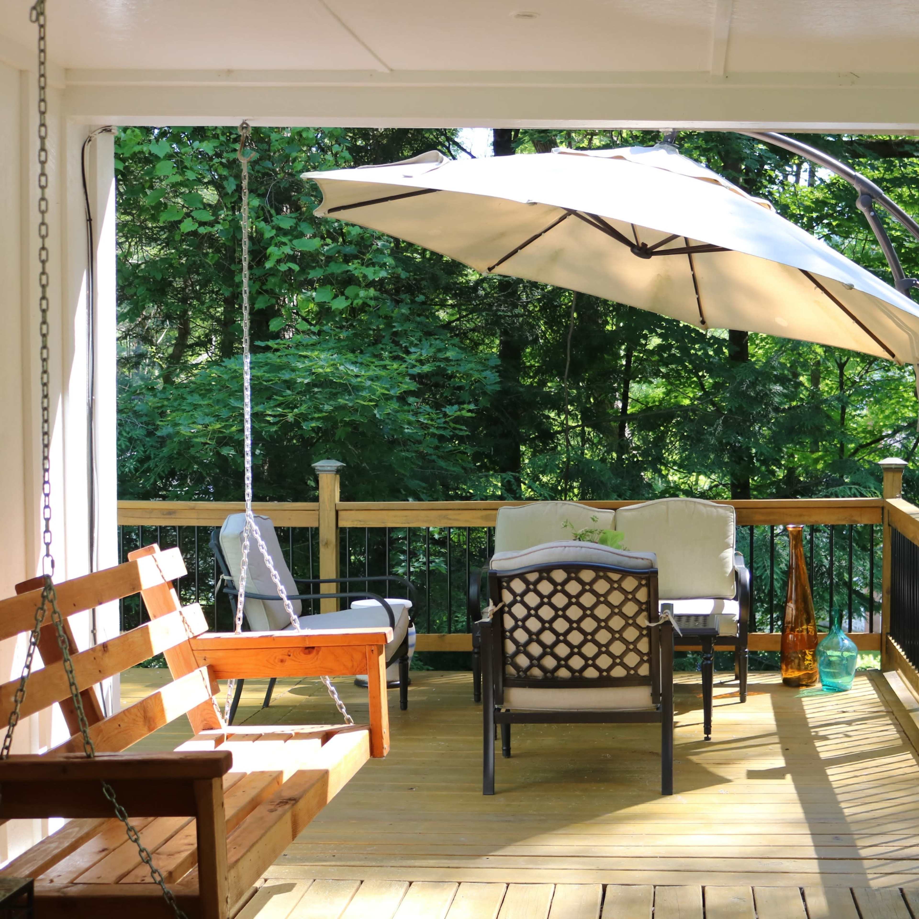 A shaded outdoor seating area features a swing and comfortable chairs surrounded by greenery.