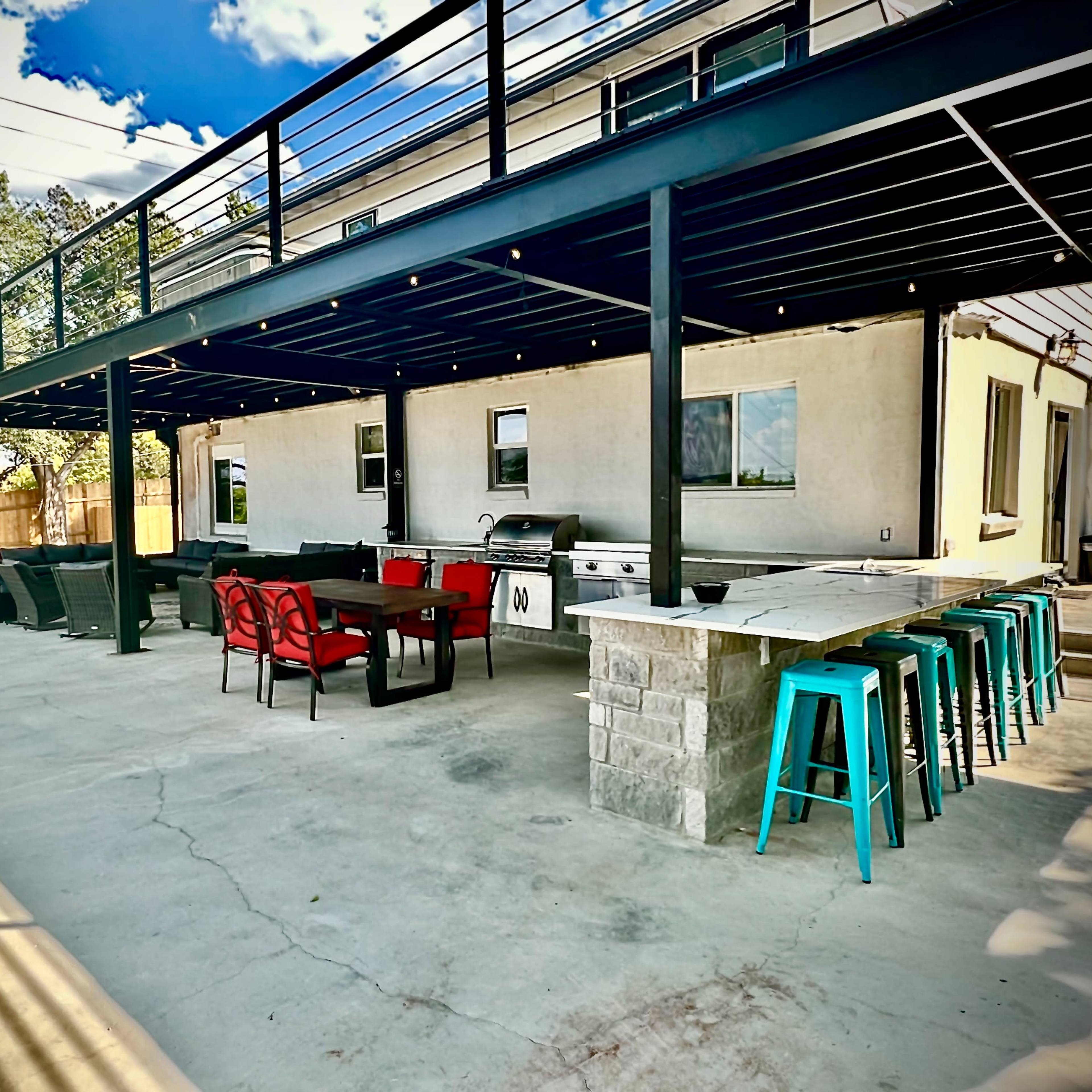 A spacious outdoor patio area with a grilling station, seating arrangements, and a covered upper deck under a clear blue sky.