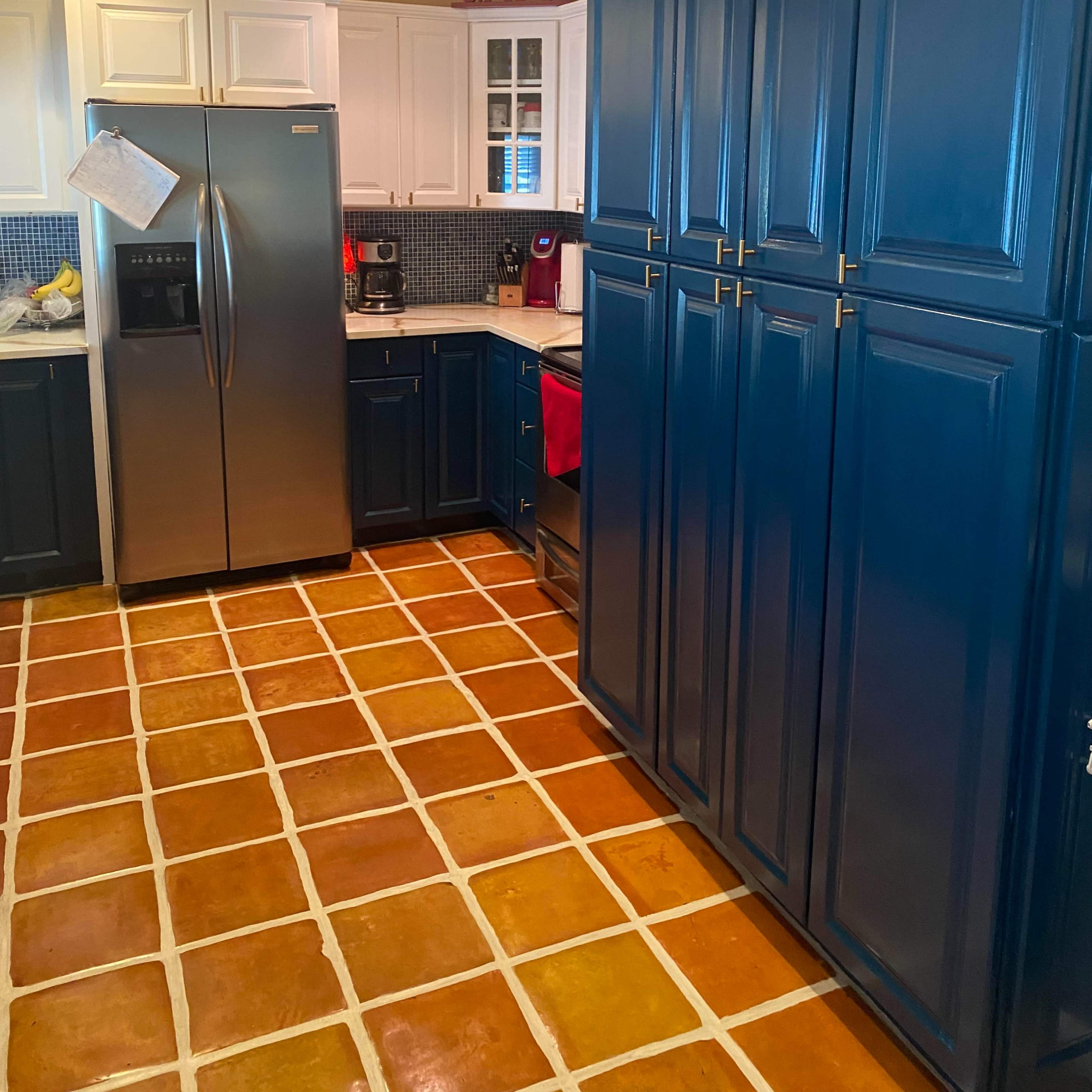 A kitchen with blue cabinetry, a stainless steel double-door refrigerator, and orange and white tiled flooring.