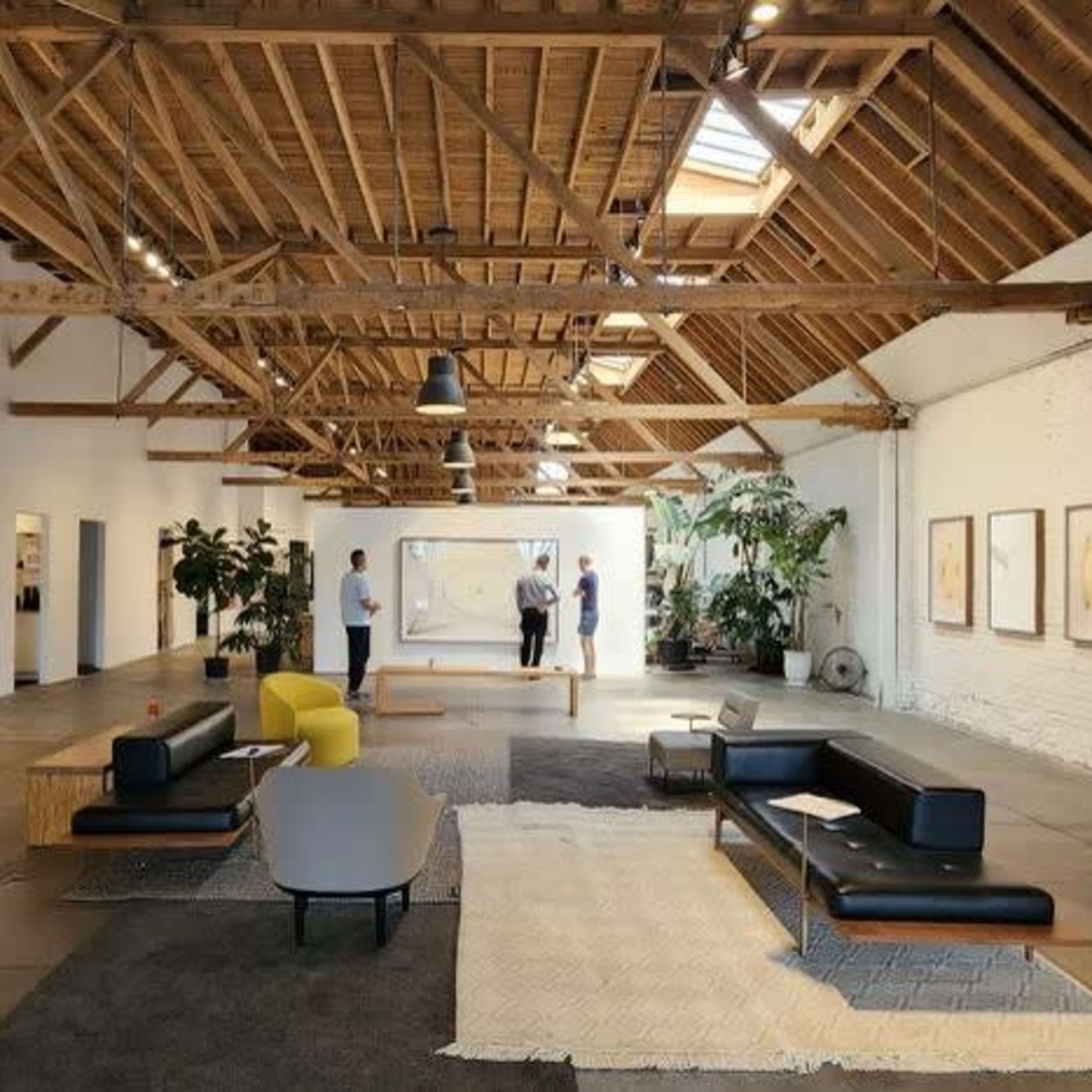 A spacious art gallery with a wooden ceiling, featuring various artworks on the walls and modern furniture arranged on the floor.