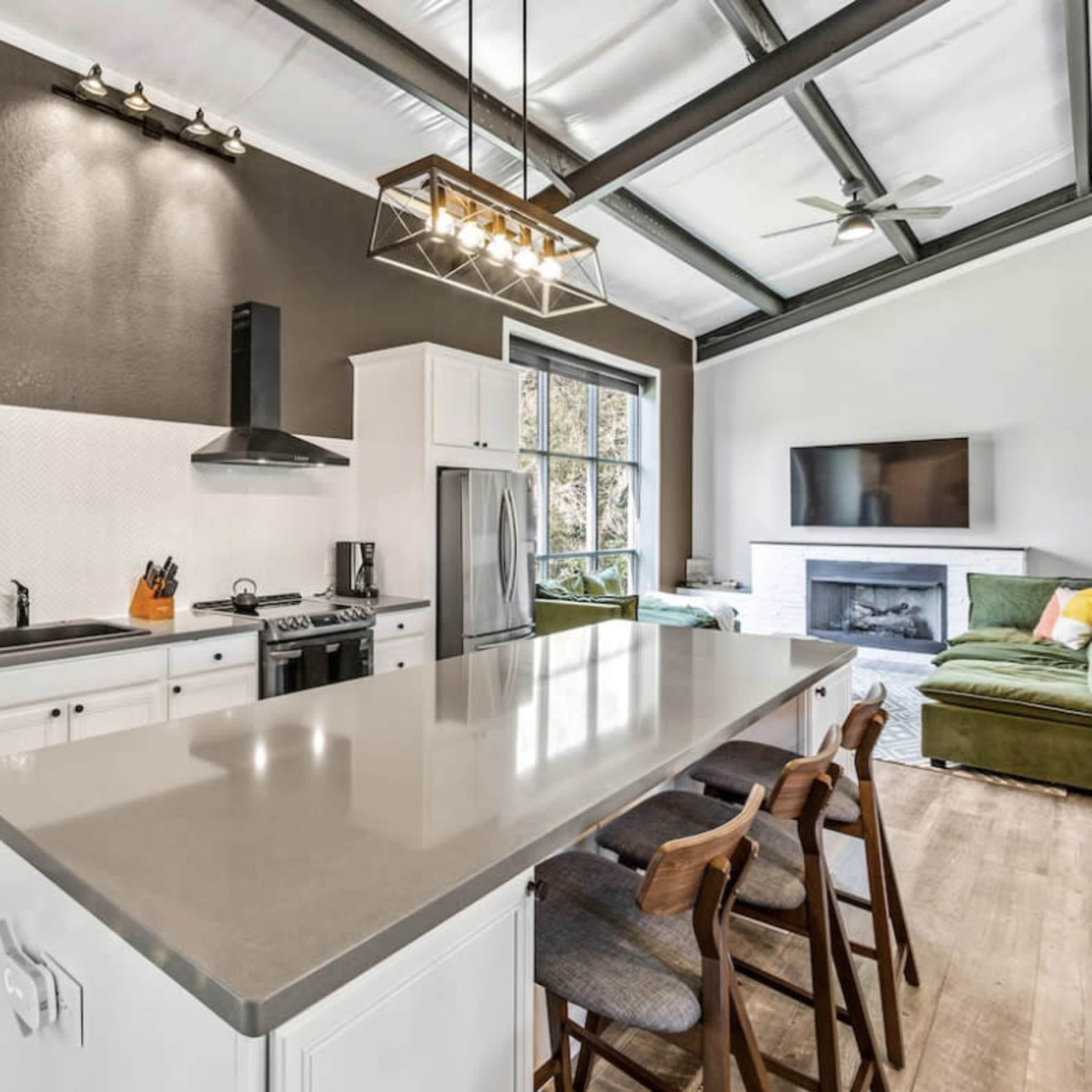 A modern kitchen with a large island, stainless steel appliances, white cabinetry, and an open layout leading to a living area.