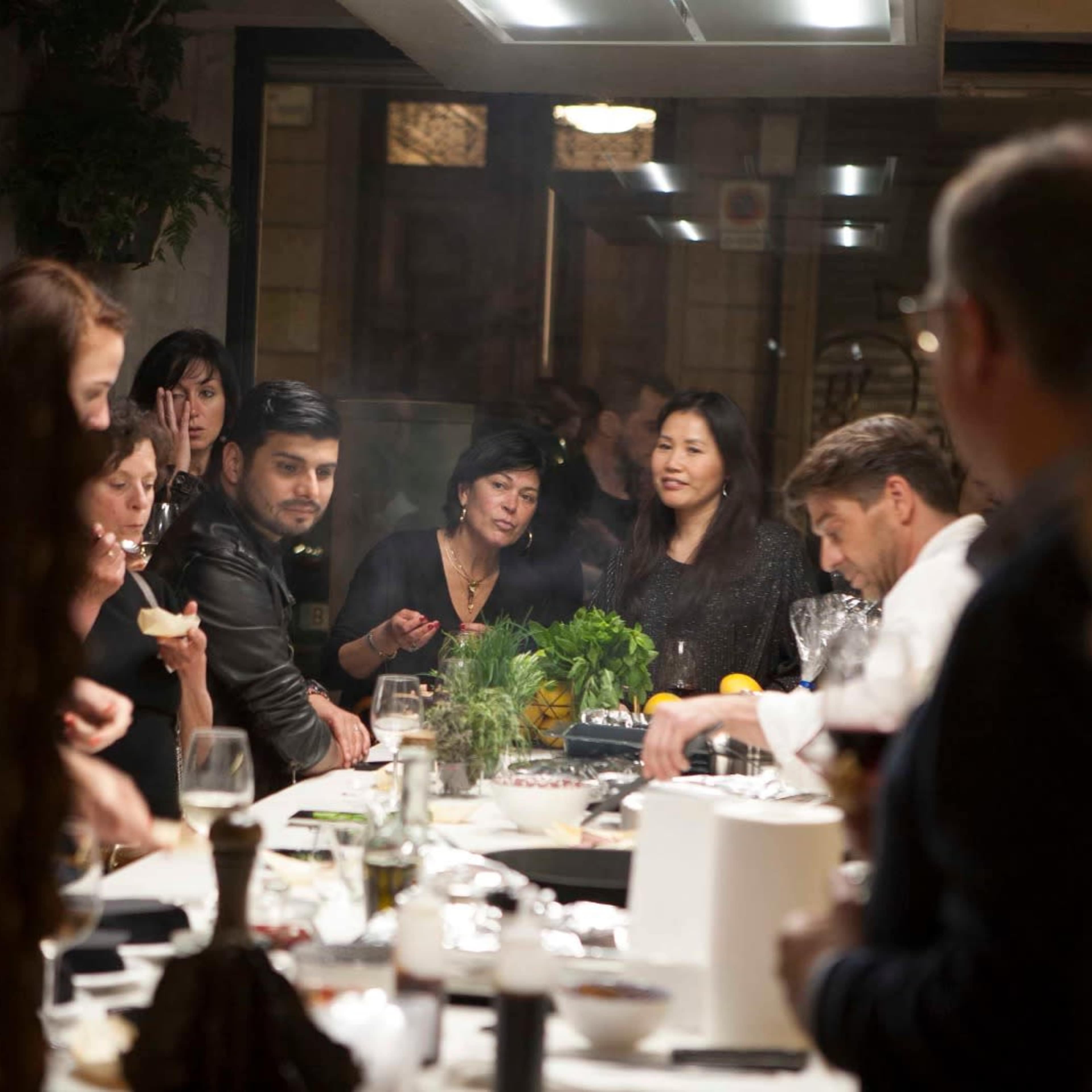 A group of people gathers around a long dining table in a well-lit restaurant, engaging in conversation while enjoying their meal.