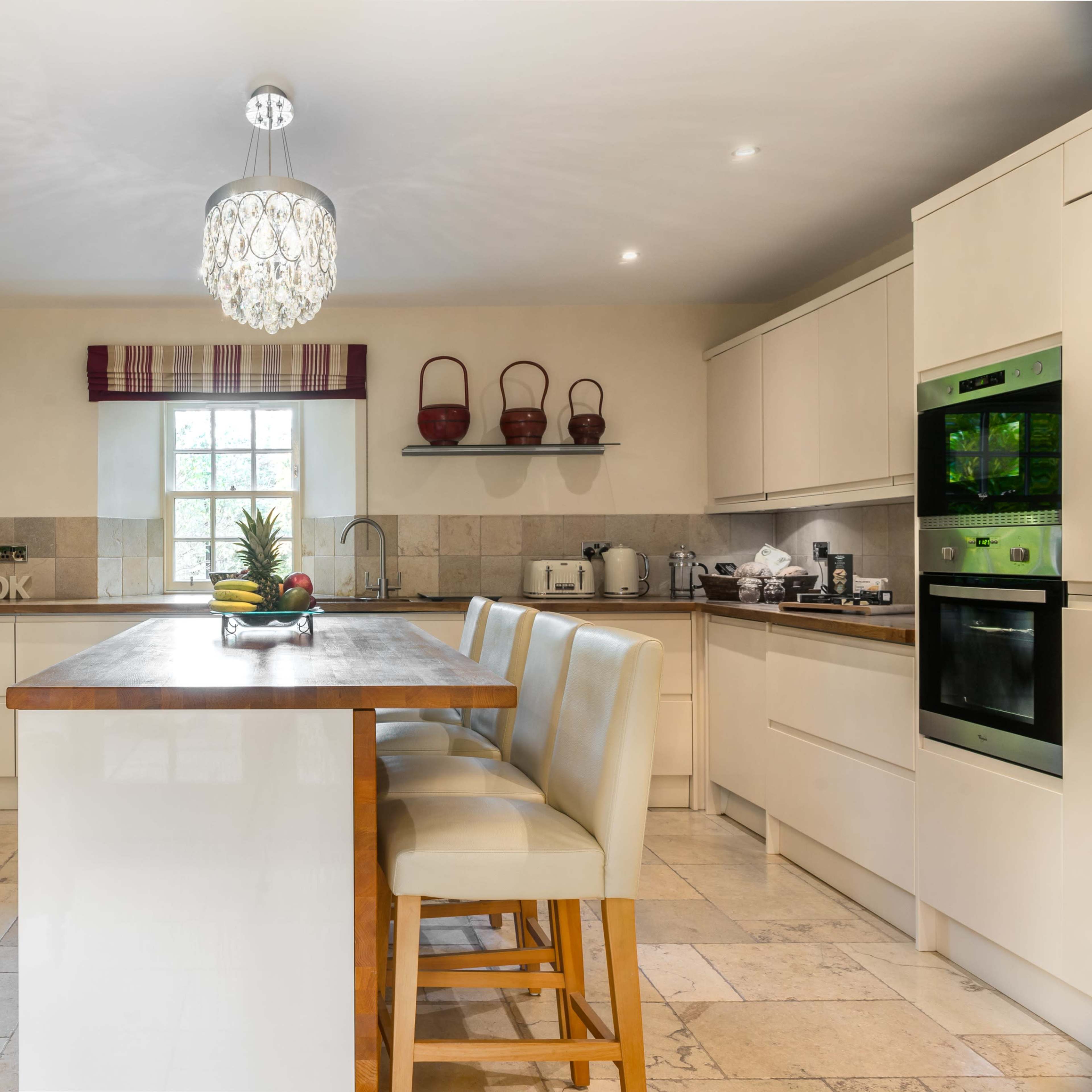 The kitchen features a central island with bar stools, an oven, and stone walls, illuminated by a chandelier.