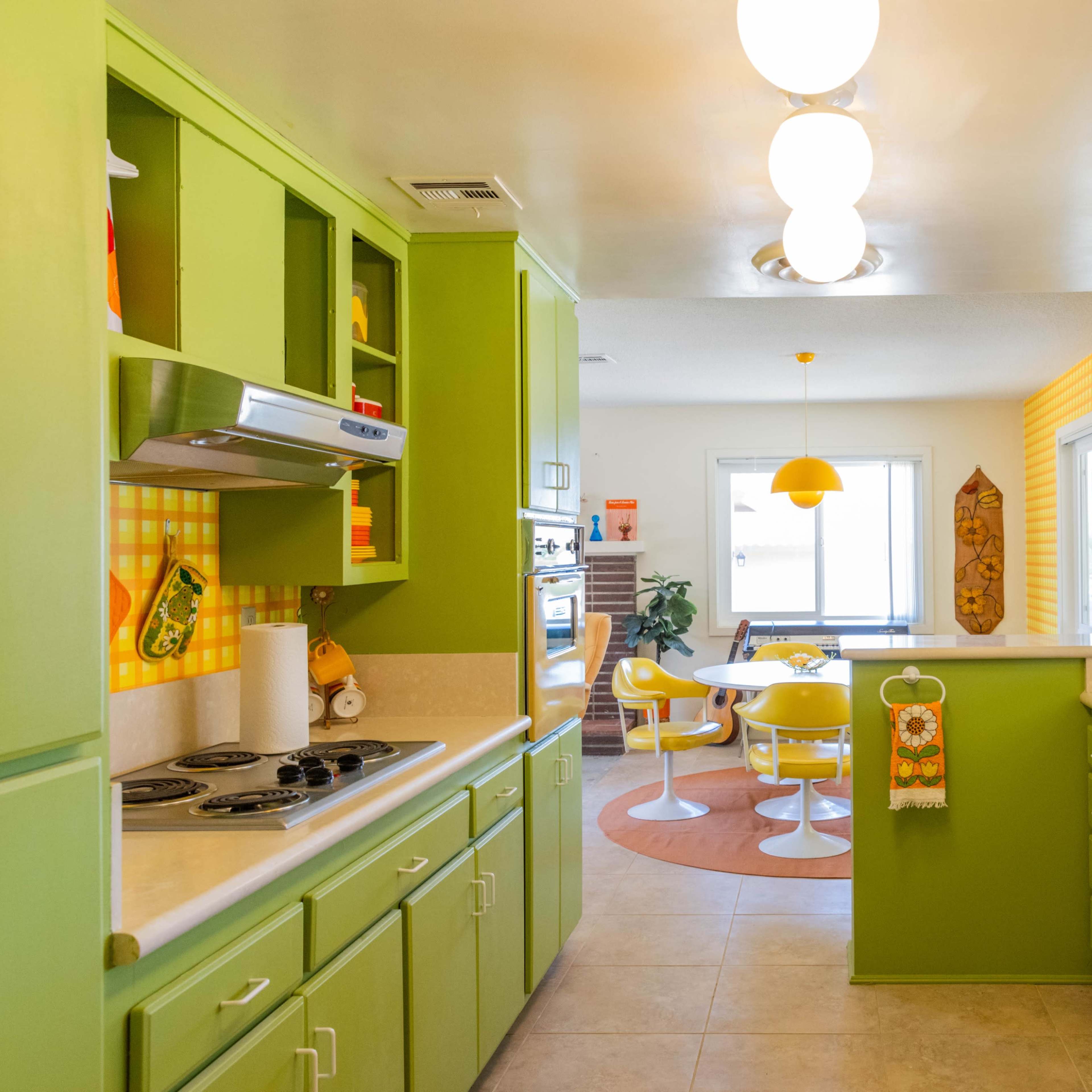A brightly colored kitchen with green cabinets, a white refrigerator, and a dining area featuring a round table with yellow chairs.
