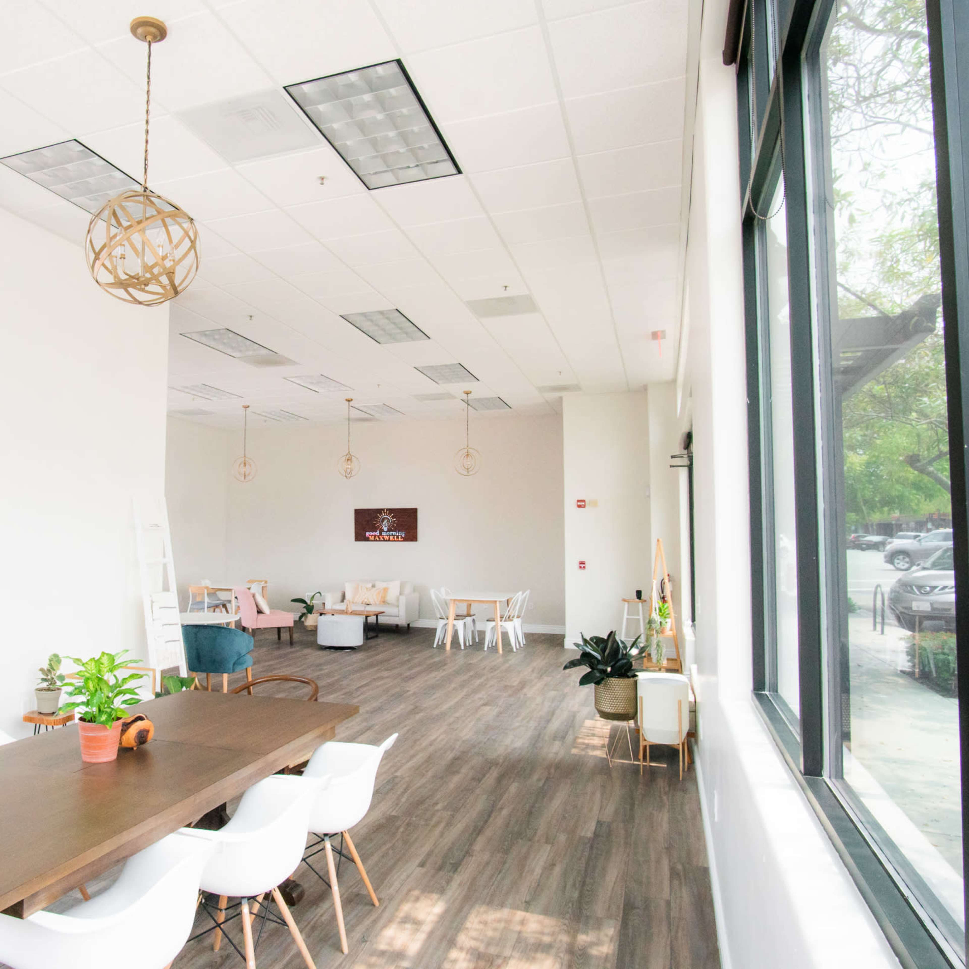 A modern, spacious interior with large windows, a long wooden dining table, and various seating arrangements.