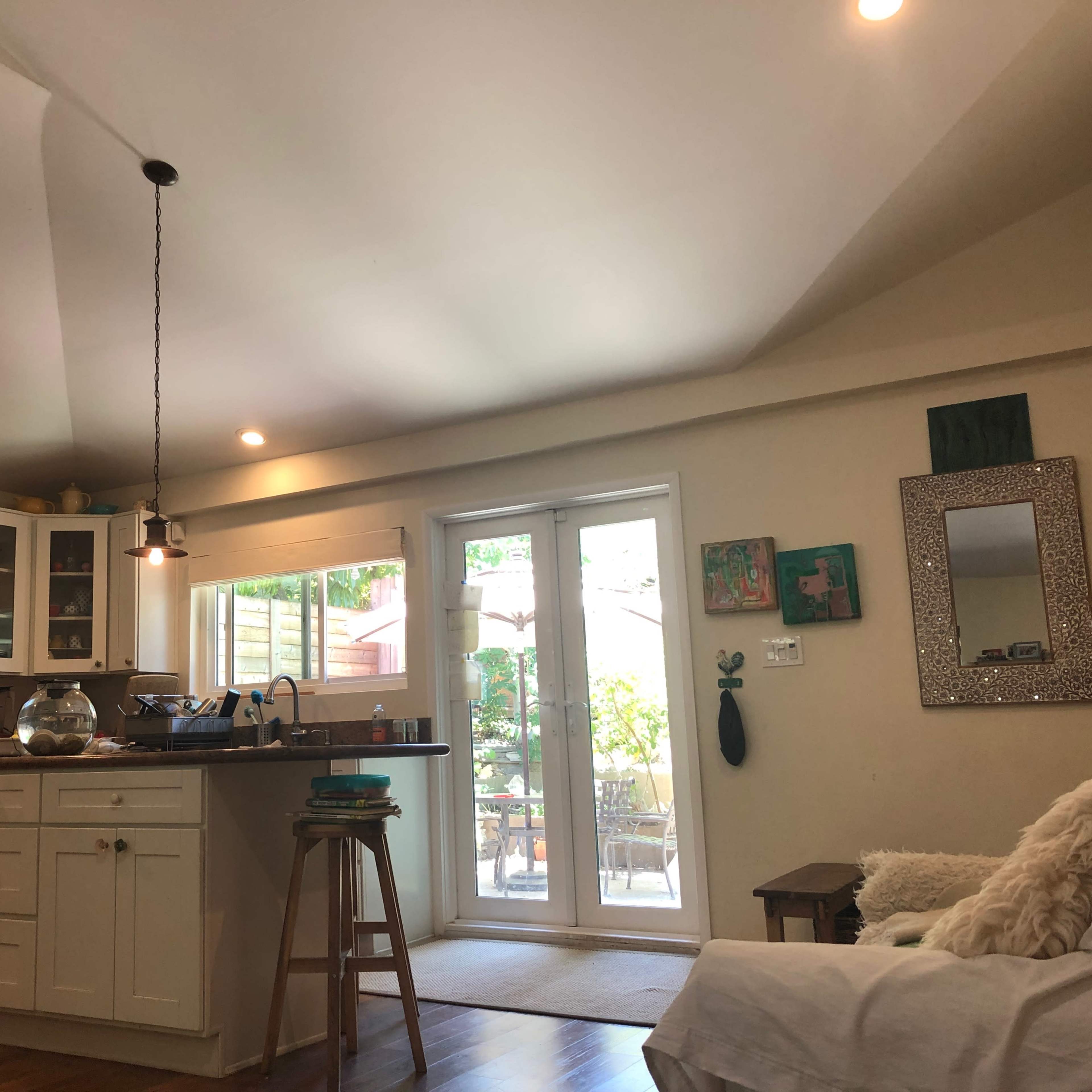A bright kitchen and dining area with white cabinets, a wooden stool, and large glass doors leading to an outdoor space.
