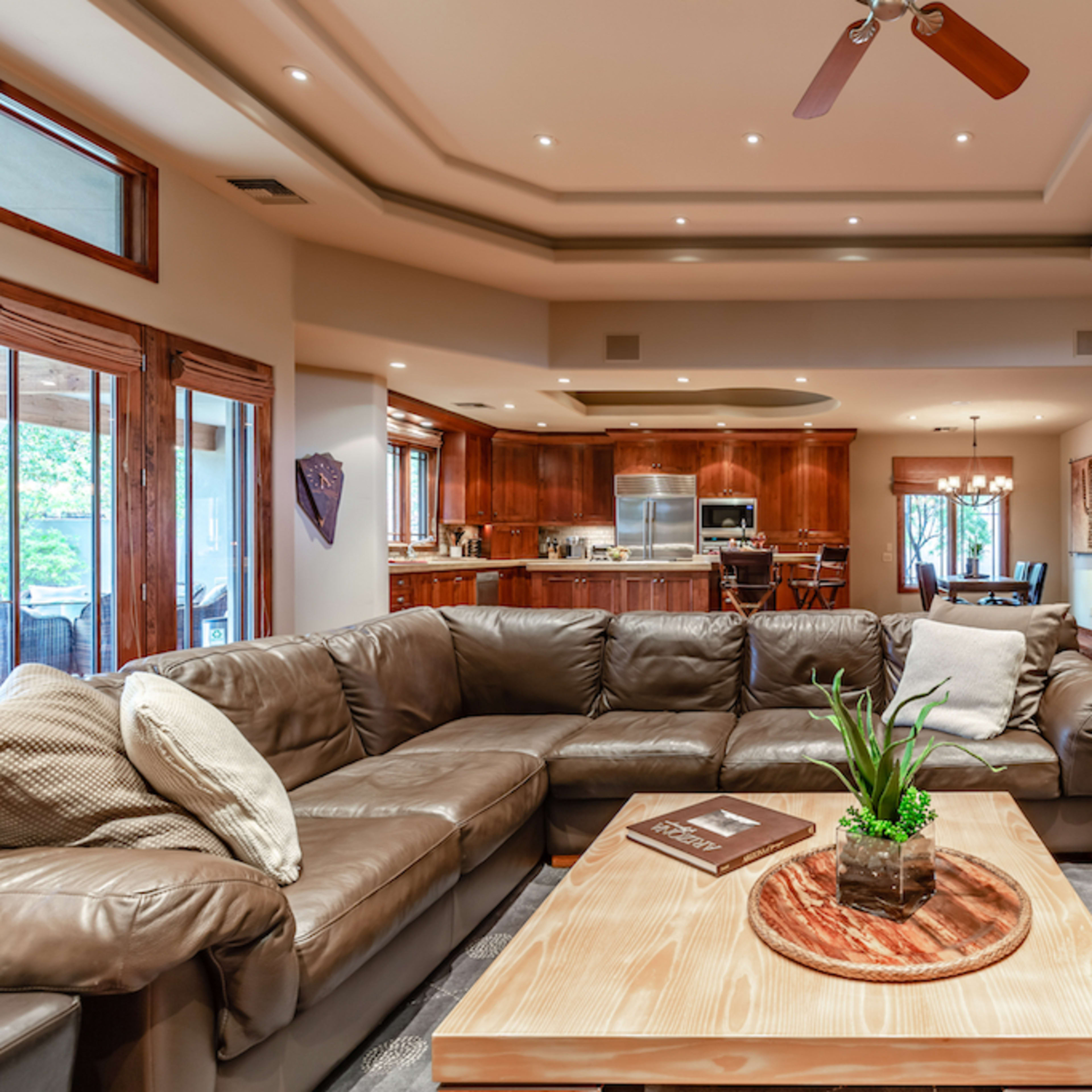 A spacious living room with a large sectional sofa, a wooden coffee table, and an open view into a modern kitchen area in the background.