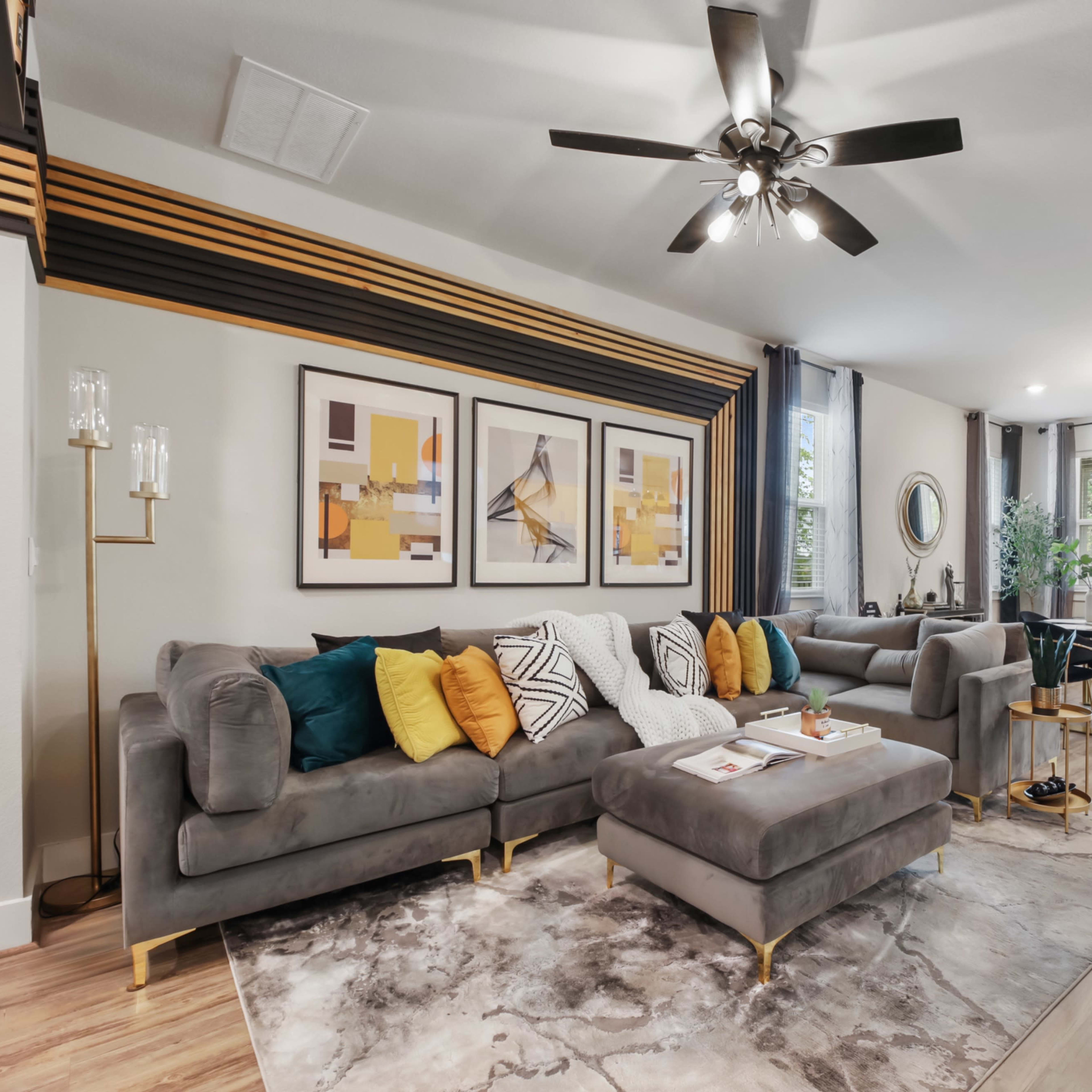 A modern living room with a gray sectional sofa, decorative cushions, a coffee table, and a dining area with a small table and chairs near large windows.