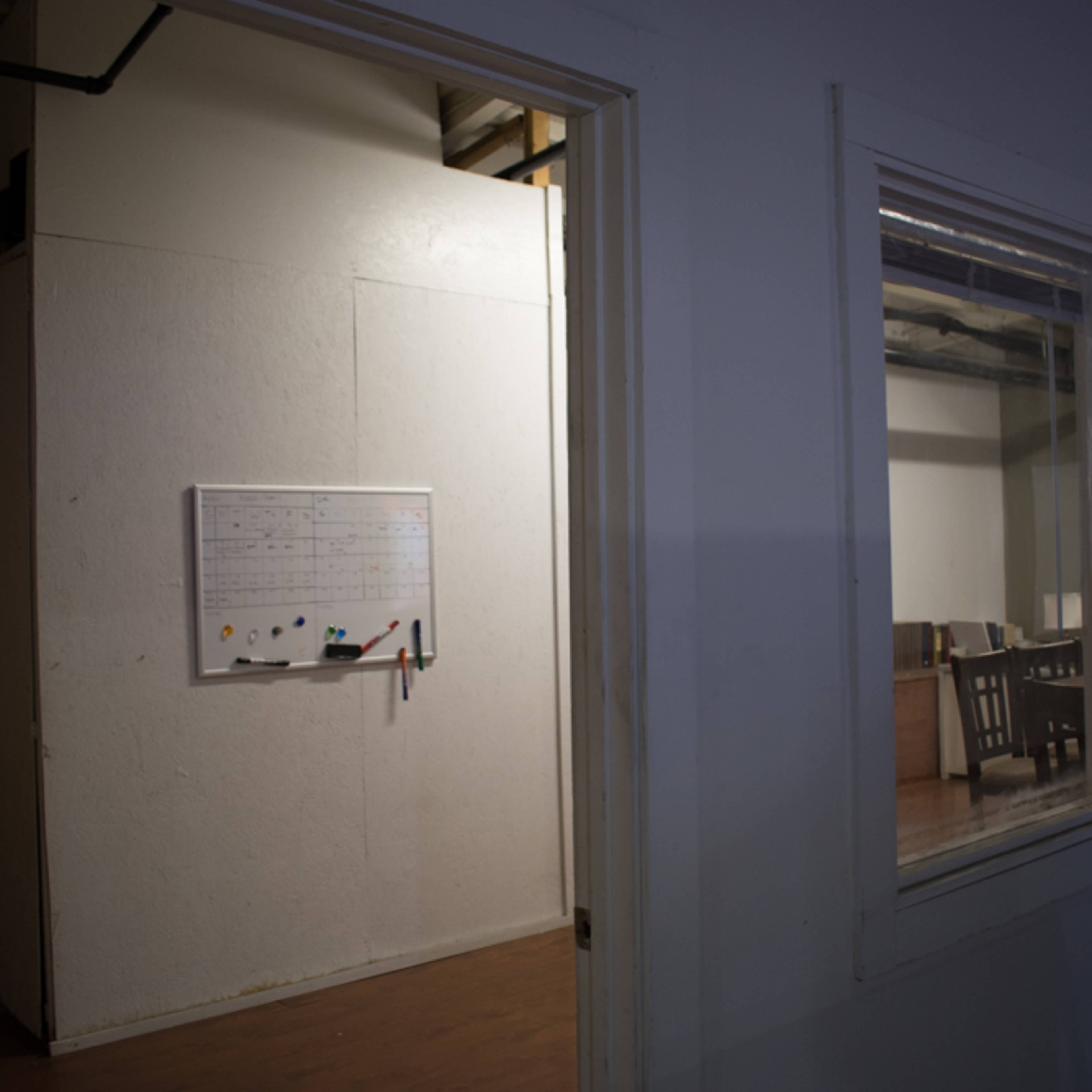 An interior view of an office space with a whiteboard mounted on a wall near an open doorway leading to another room with furniture.