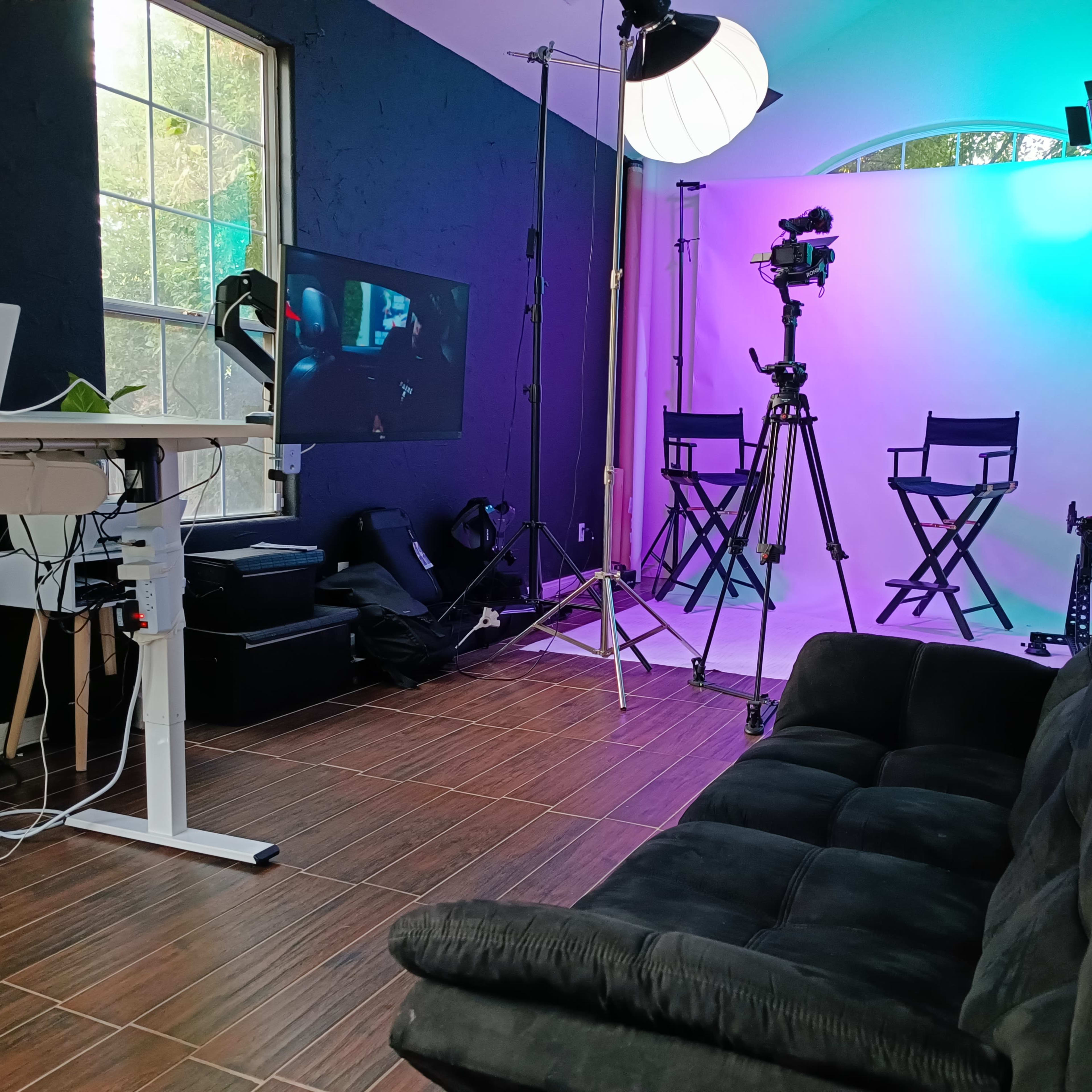 A studio setup with a black couch, two director's chairs, video cameras, and lighting equipment in front of a colorful backdrop.