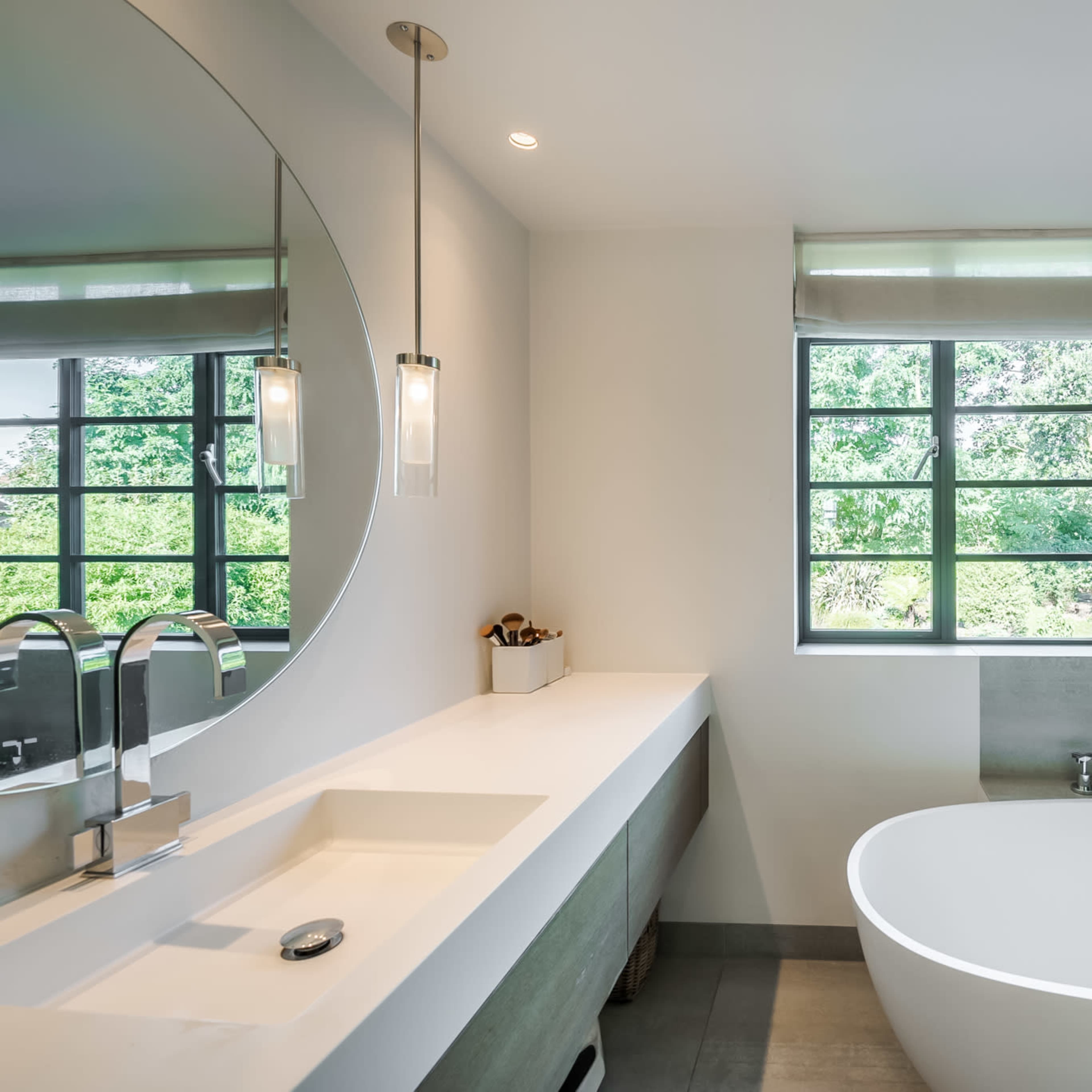 The bathroom features a freestanding oval bathtub, a modern sink with a mirror, and a window overlooking an outdoor green landscape.