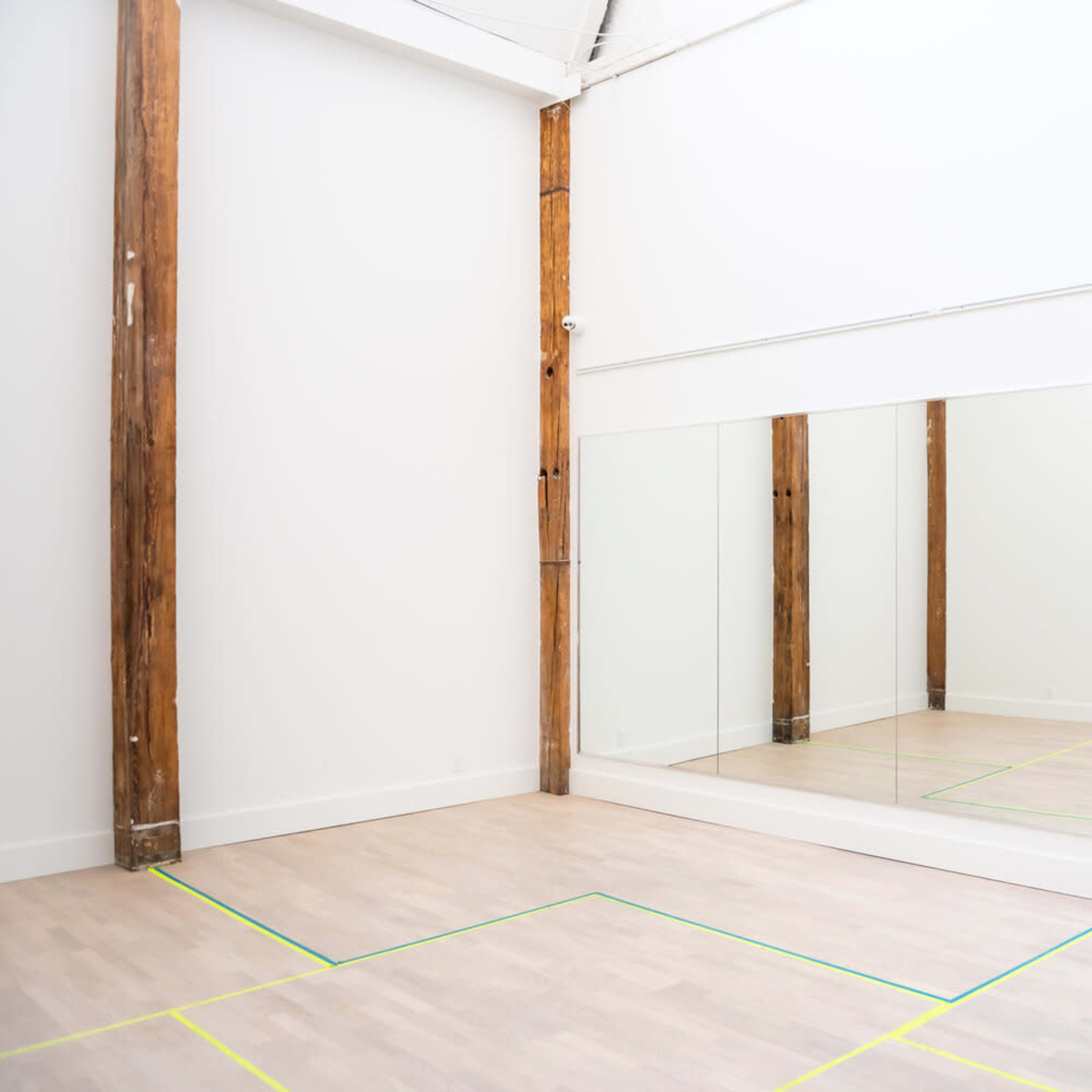 A spacious room with wooden beams, a large mirror on one wall, and marked lines on the floor, indicating a practice or workout area.