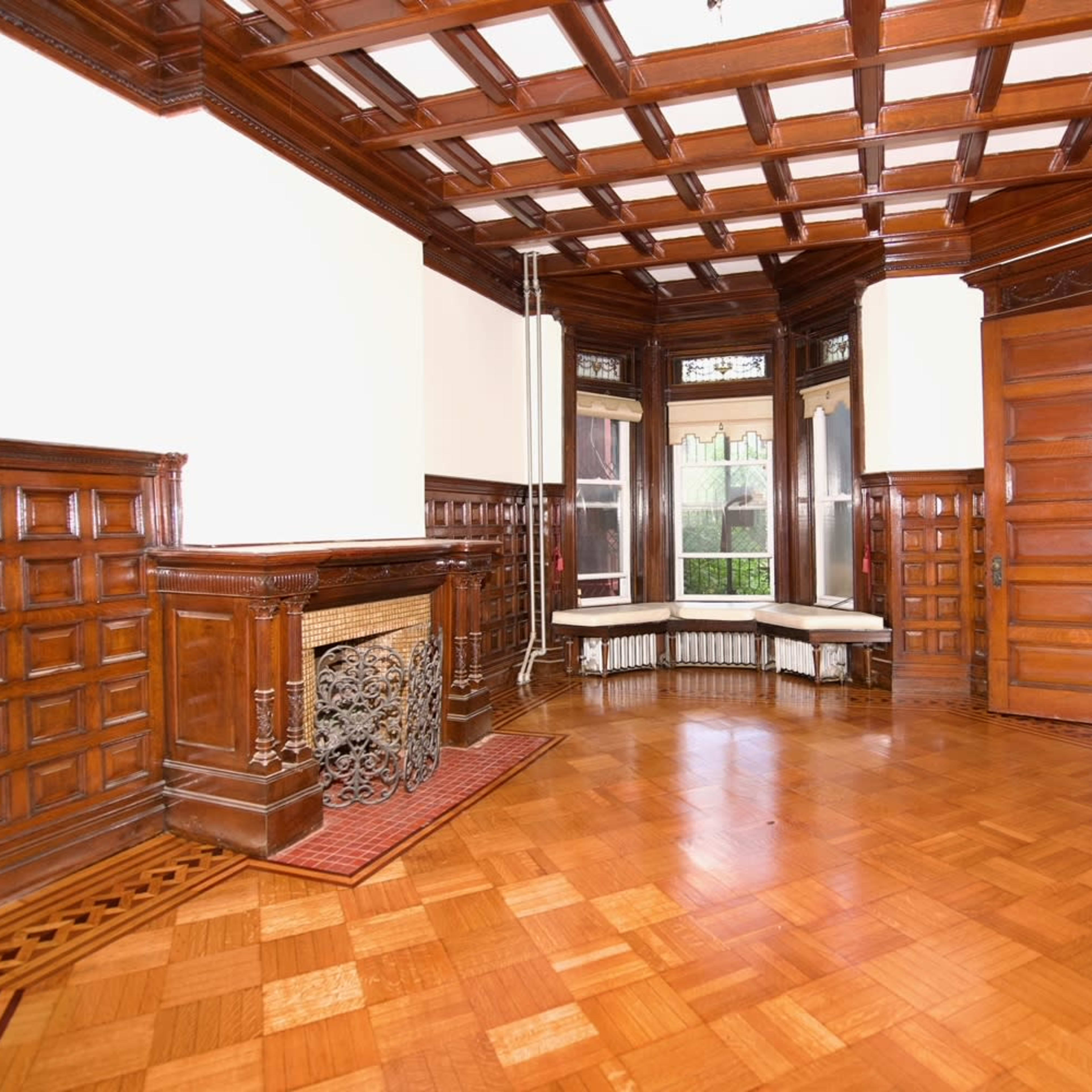 A wooden-paneled room with a coffered ceiling, featuring a fireplace and three large windows.