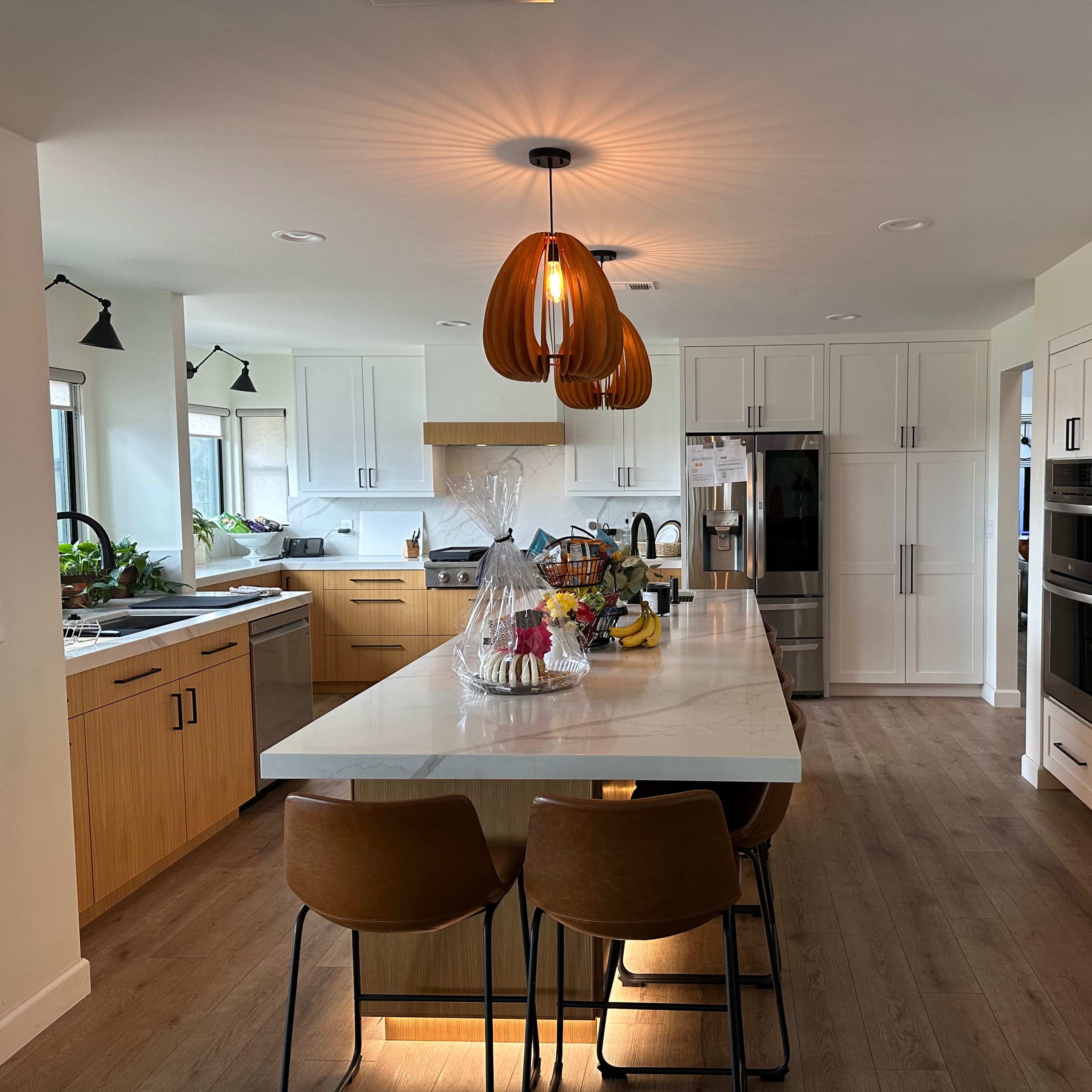 A modern kitchen with white cabinetry, wooden accents, a large island with seating, and pendant lighting above.