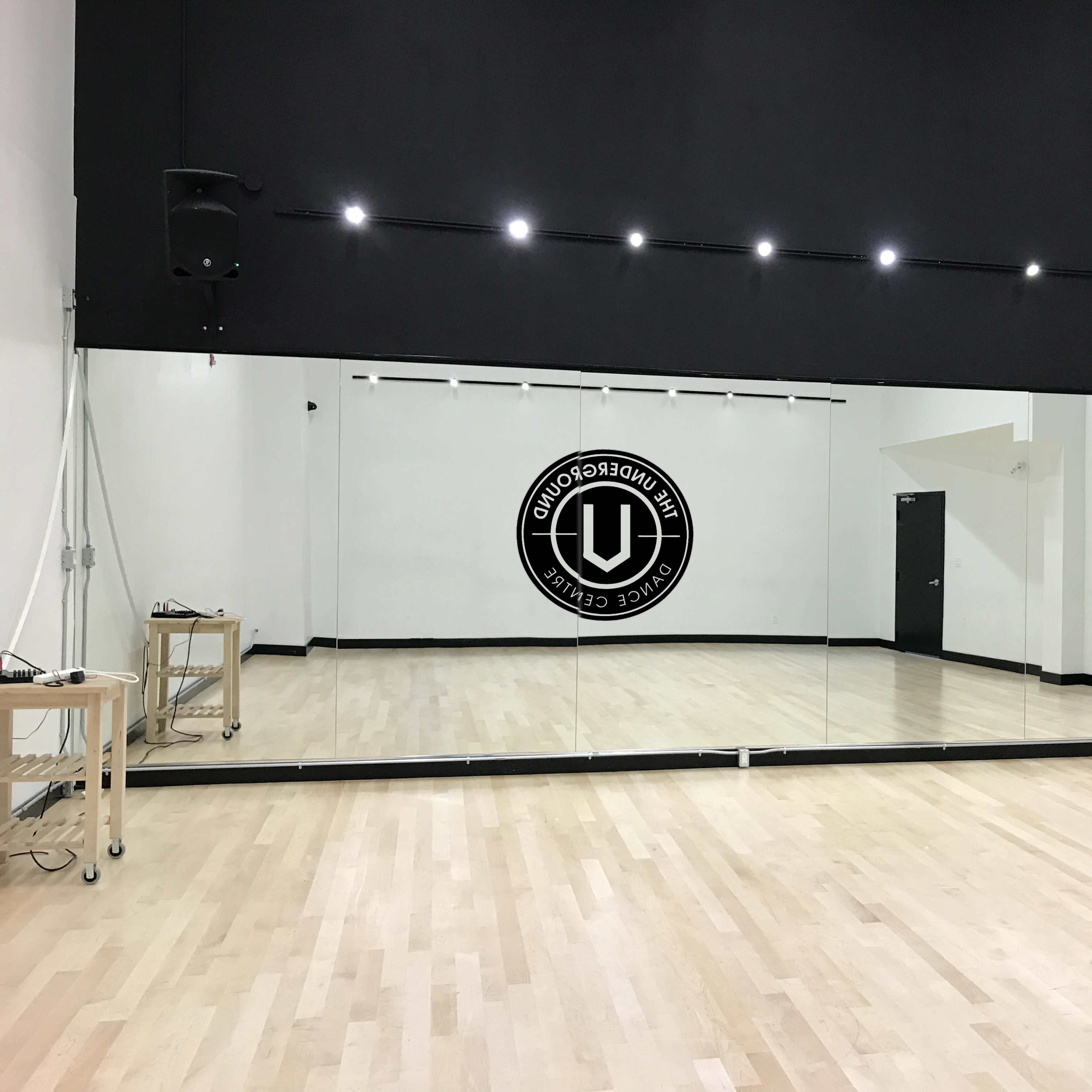 A spacious dance studio with a large mirrored wall and a logo on the back wall.