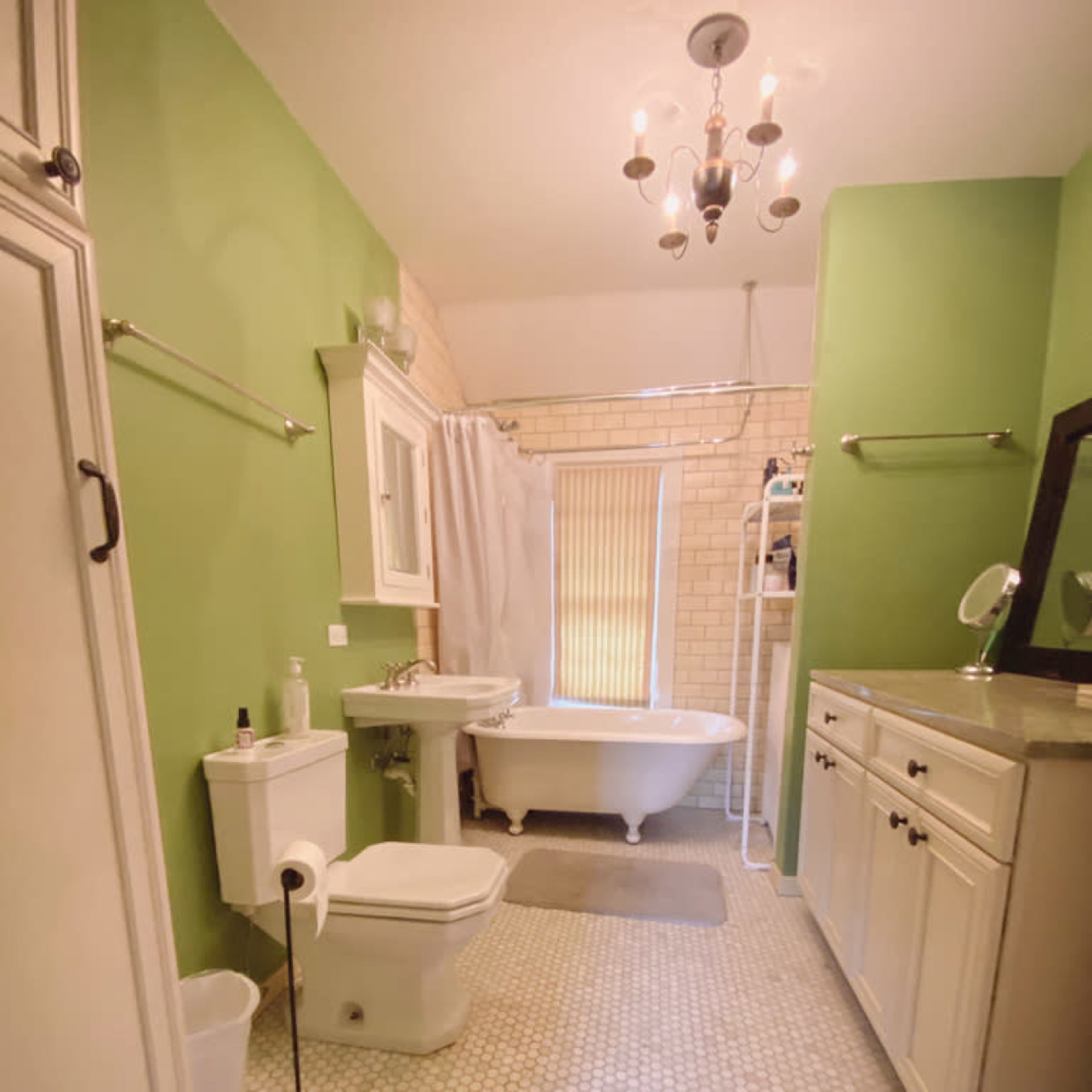 The bathroom features a vintage bathtub, a white toilet, and a sink with a mirror, all set against green walls and hexagonal tile flooring.