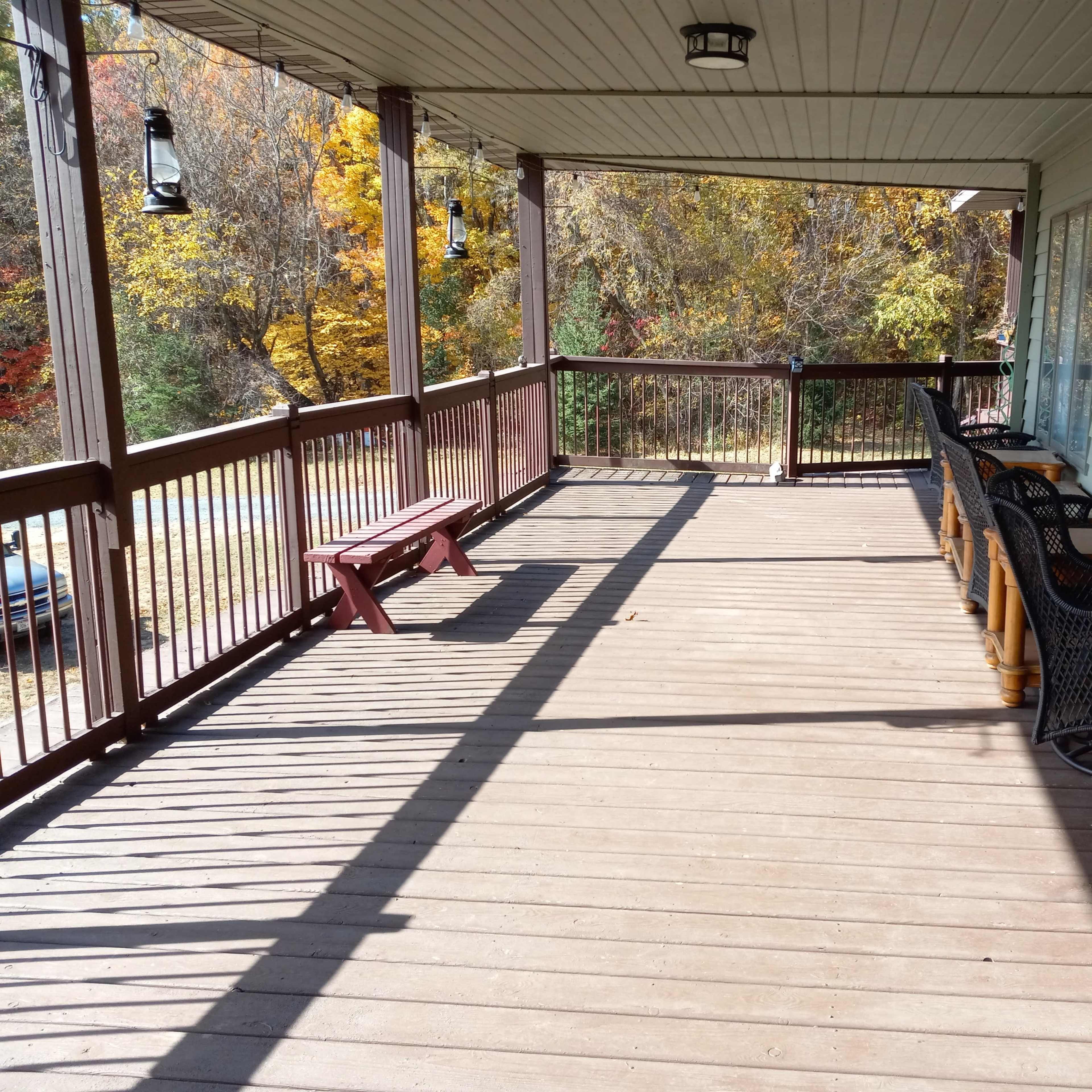 A wooden porch with a bench, several chairs, and autumn foliage visible in the background.