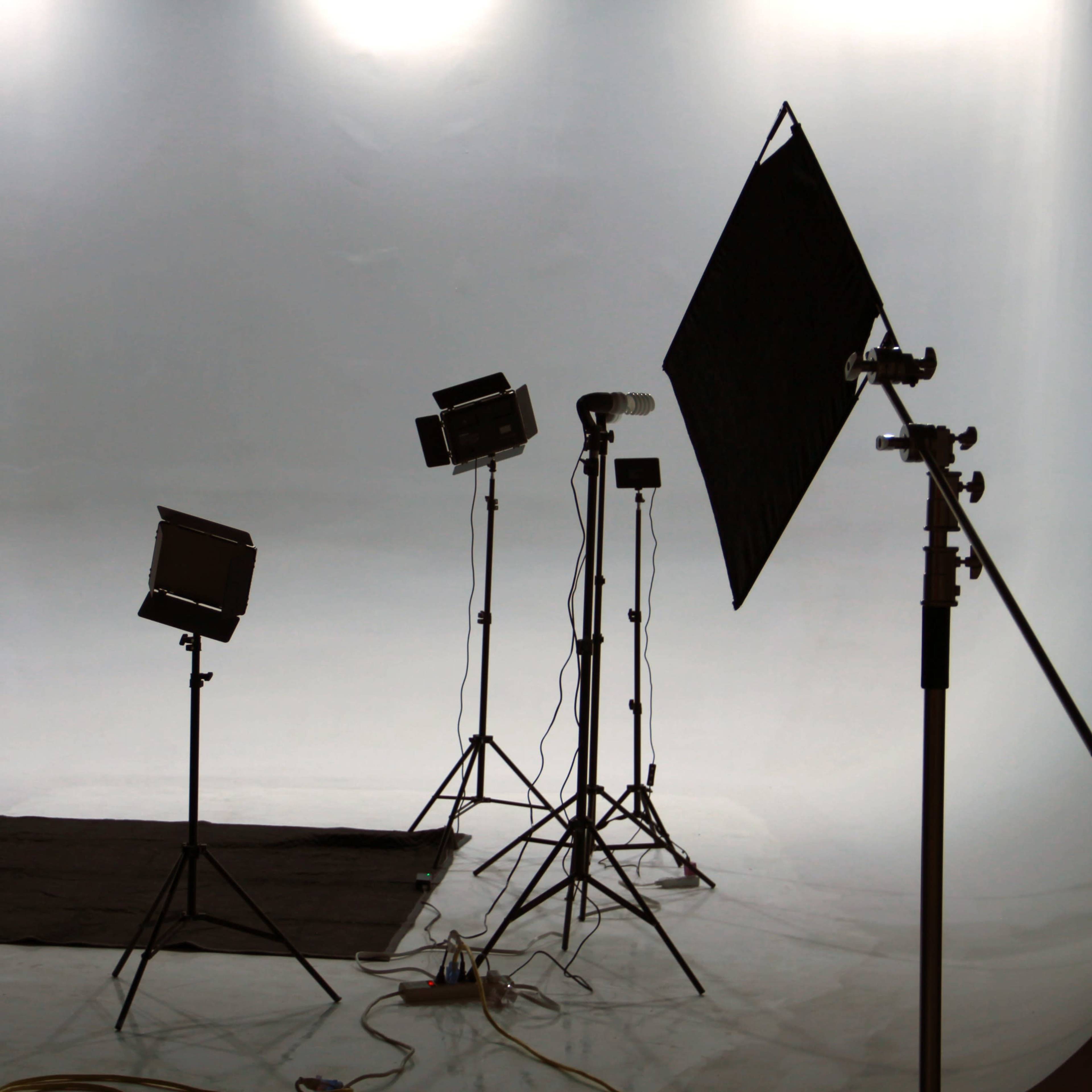A photo studio setup with lighting equipment and a blank backdrop.