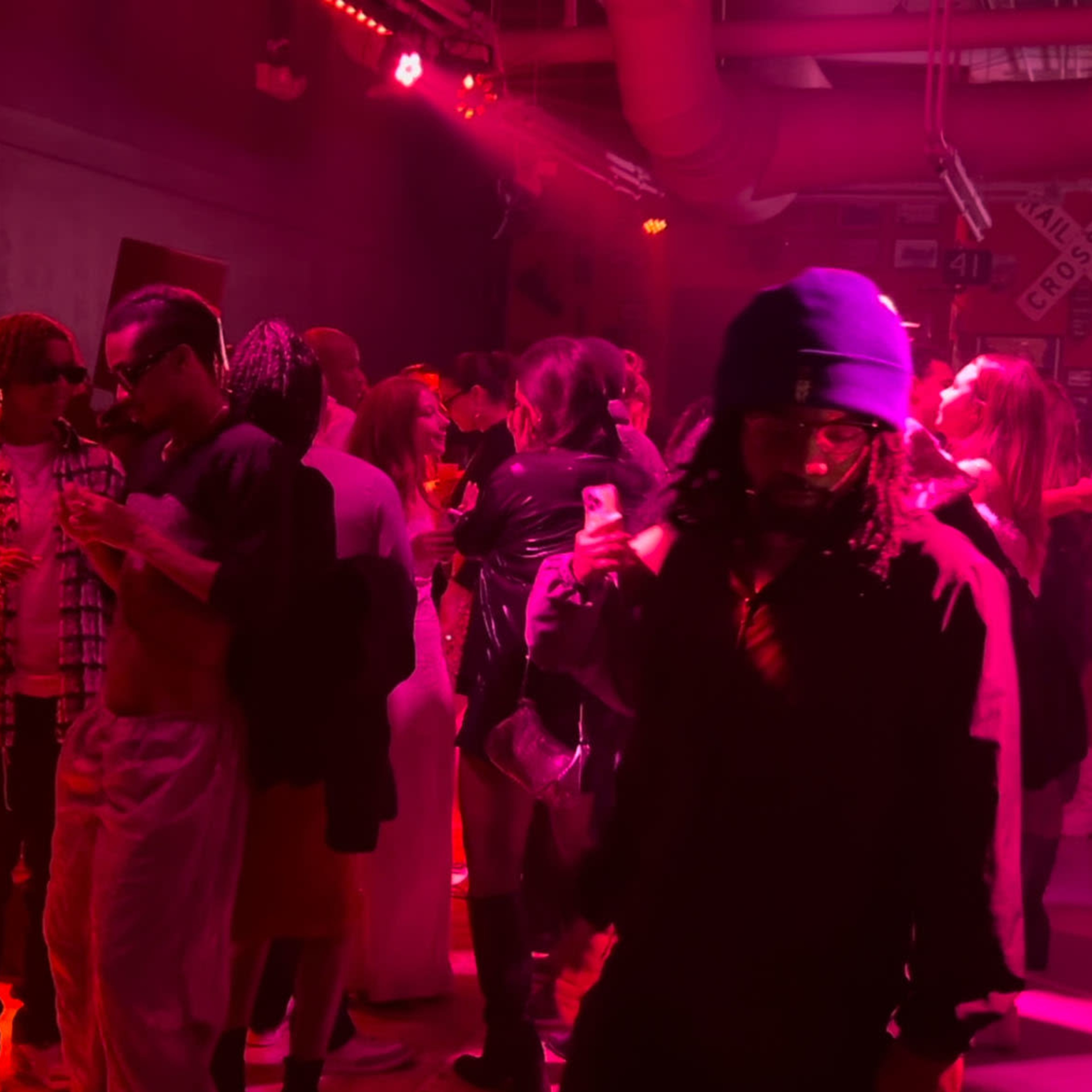A crowd of people gathers in a dimly lit room with red lighting, engaged in conversation and mingling during an event.