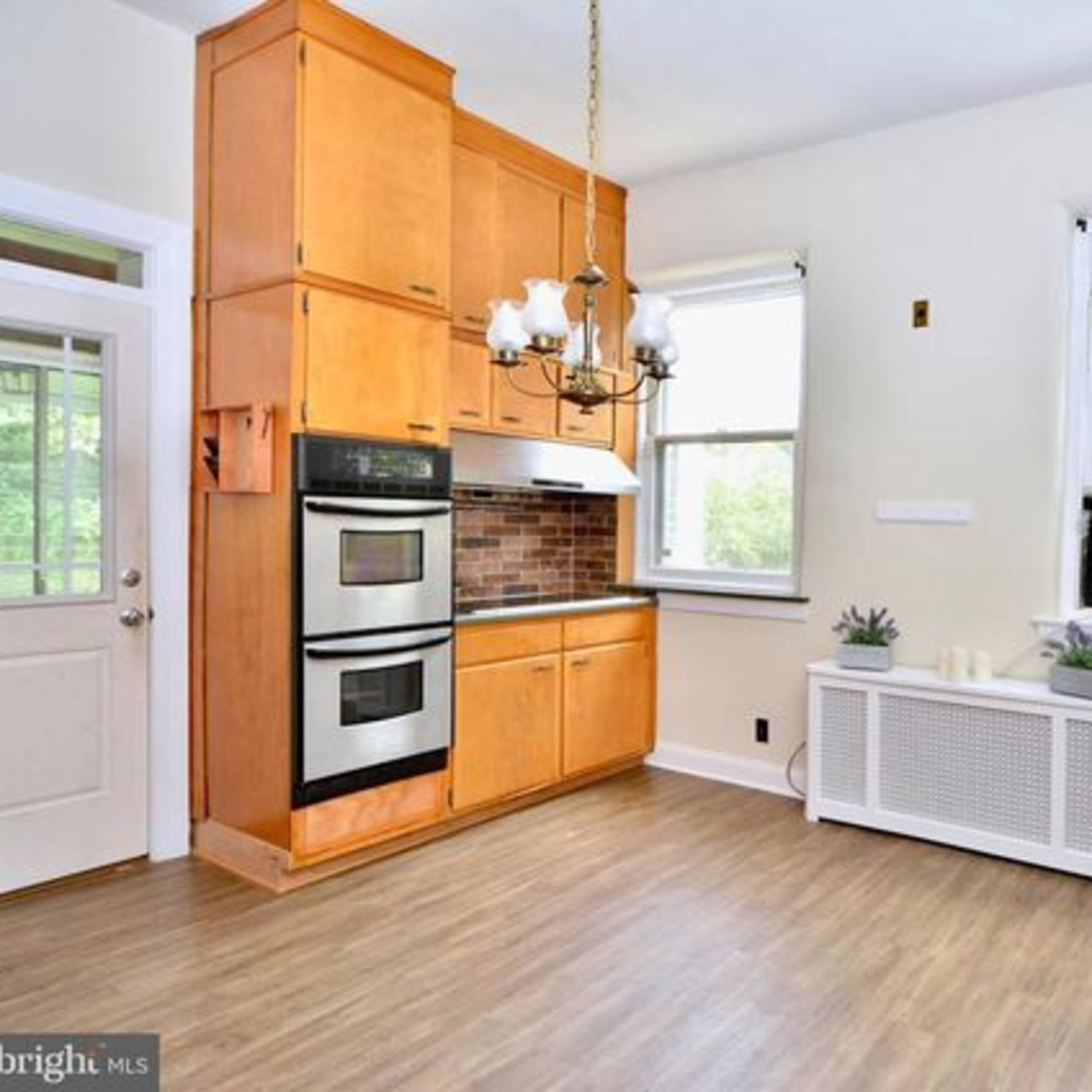 A bright kitchen featuring wooden cabinetry, an oven, and an air conditioning unit beneath a window.