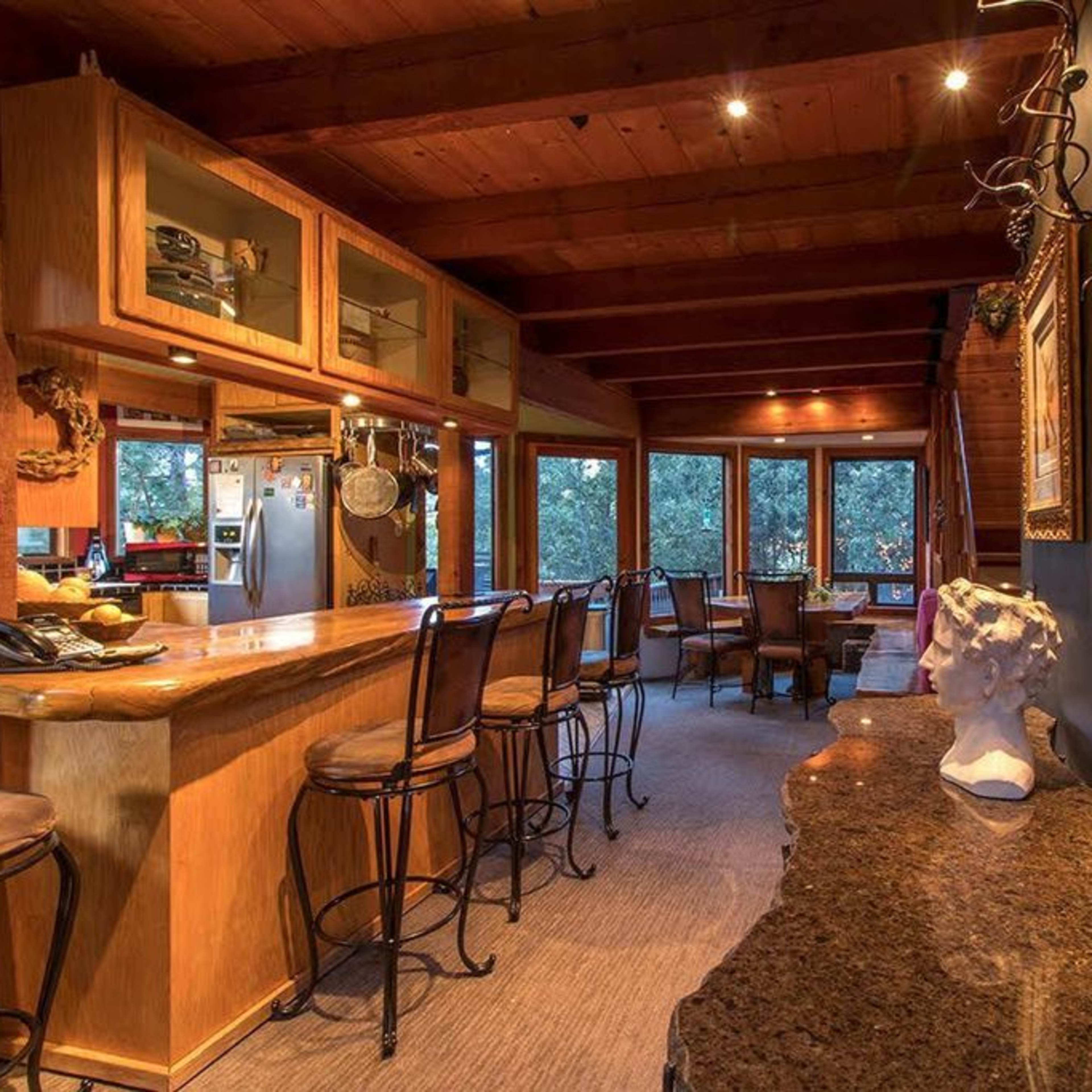 A wooden-themed kitchen and dining area with bar seating, large windows, and a sculpture on a granite surface.