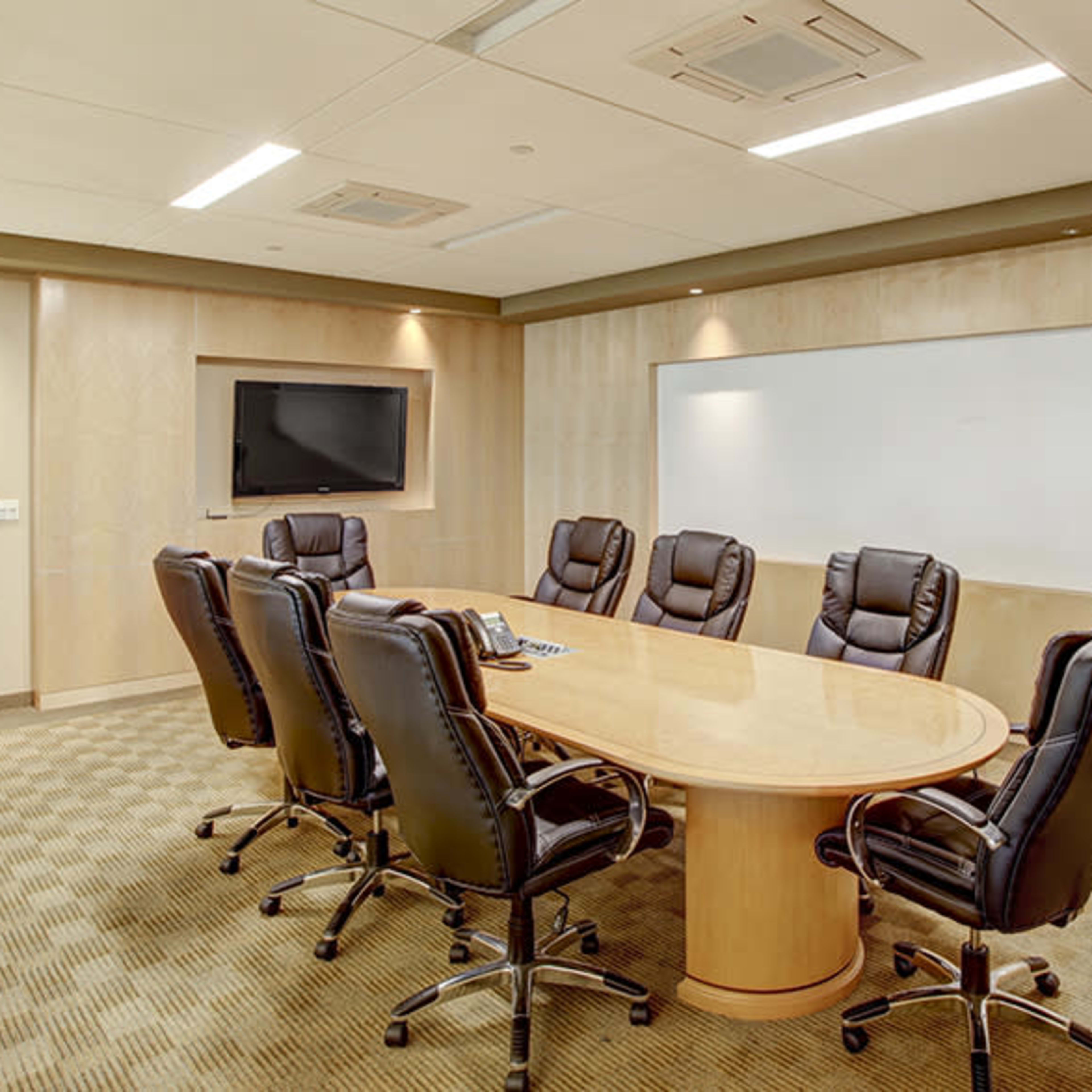 A modern conference room features a large oval table surrounded by eight executive chairs, with a whiteboard and a TV mounted on the wall.