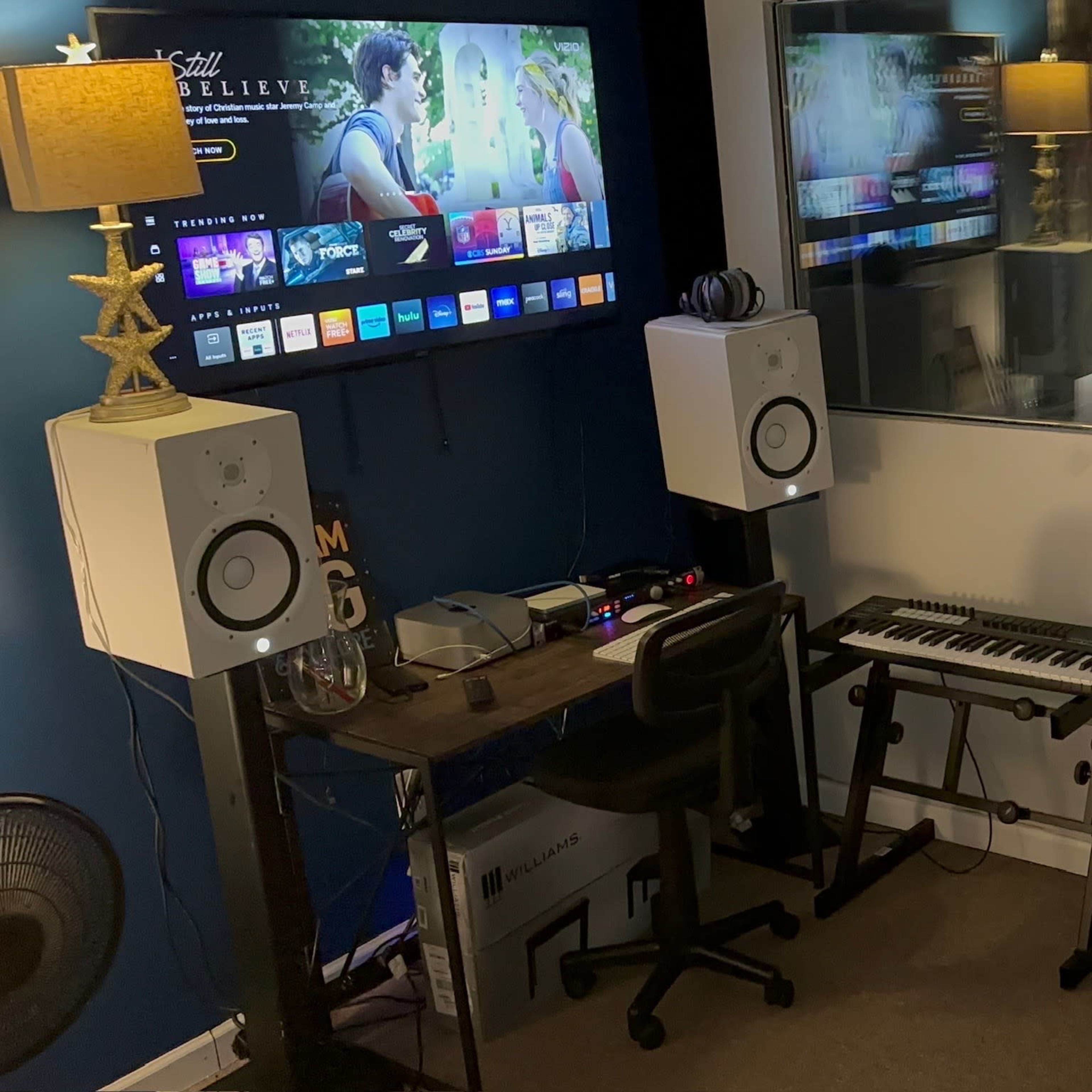 A small room features a large TV on one wall, a desk with a keyboard and computer equipment, and a sofa facing the screen.